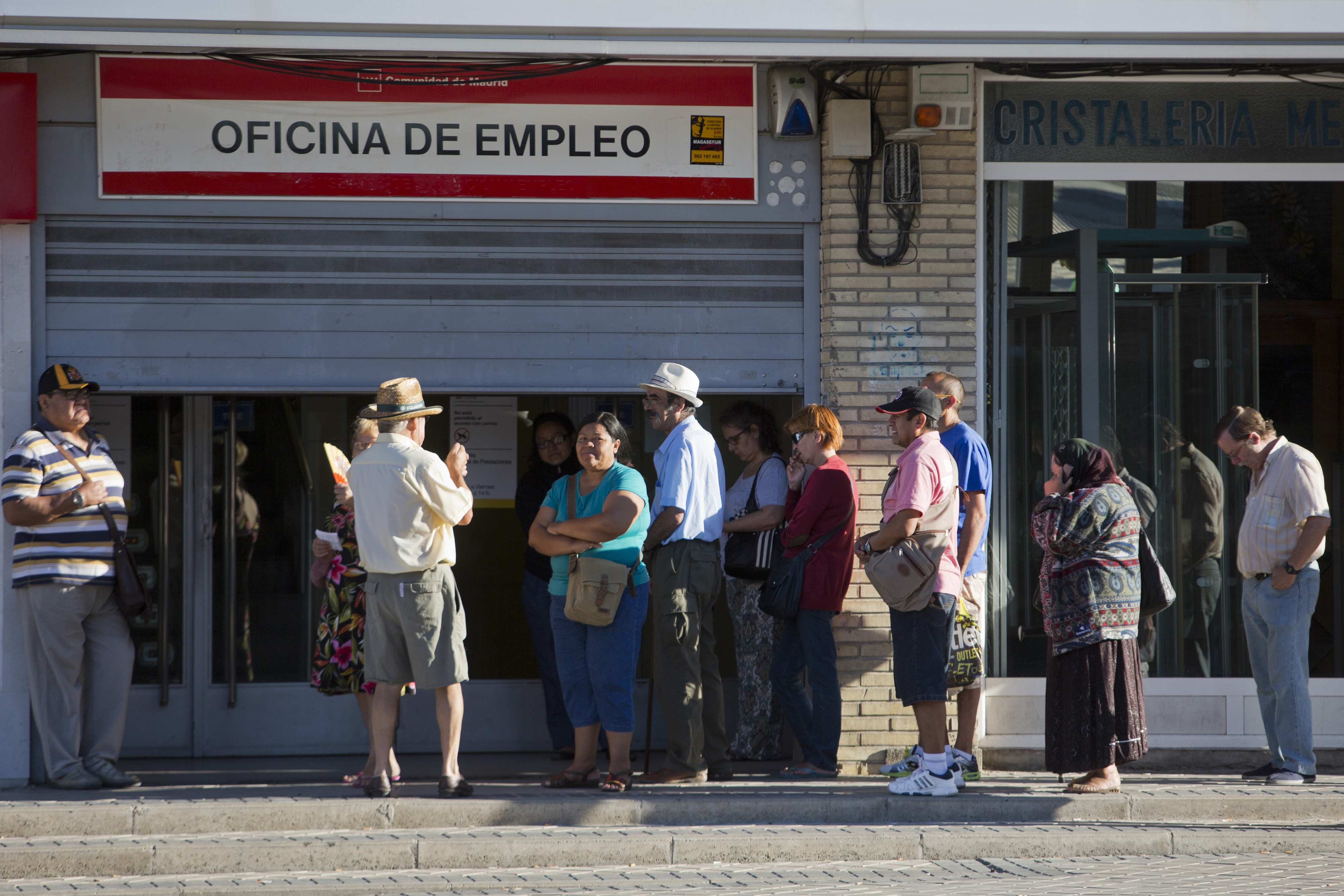 Jobseekers queue outside the shuttered entrance to an employment center shortly before opening in Madrid, Spain, on Wednesday, July 23, 2014. While unemployment figures tomorrow will show that about a quarter of the workforce remains jobless, the government expects GDP to gain 1.2 percent this year after shrinking as much in 2013. Photographer: Angel Navarrete/Bloomberg via Getty Images