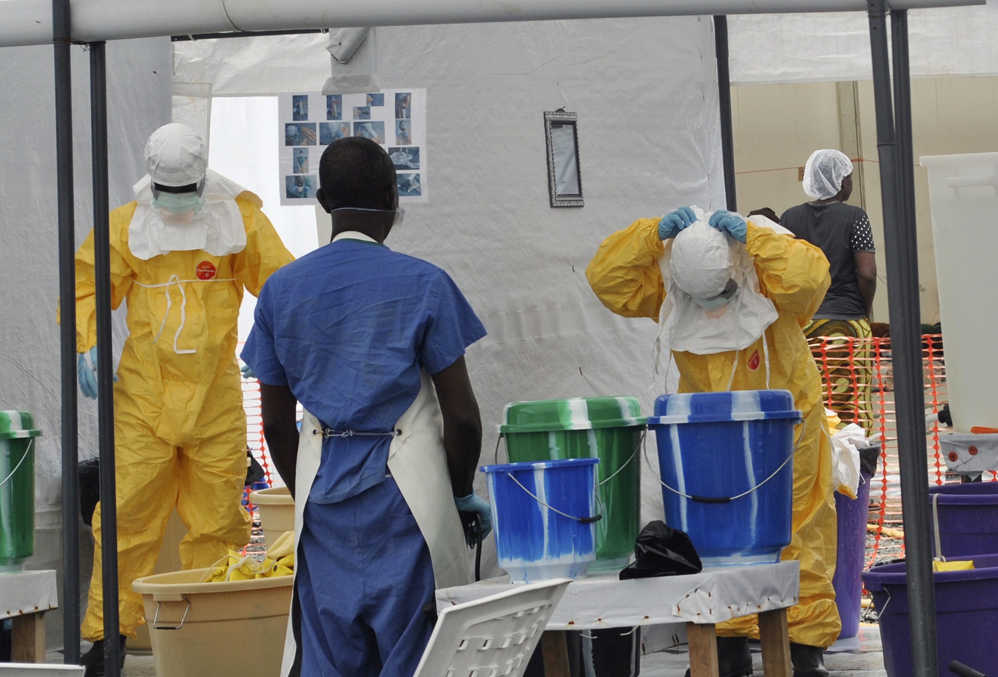 A Doctors Without Borders health worker takes off his protective gear under the surveillance of a colleague at a treatment facility for Ebola victims in Monrovia