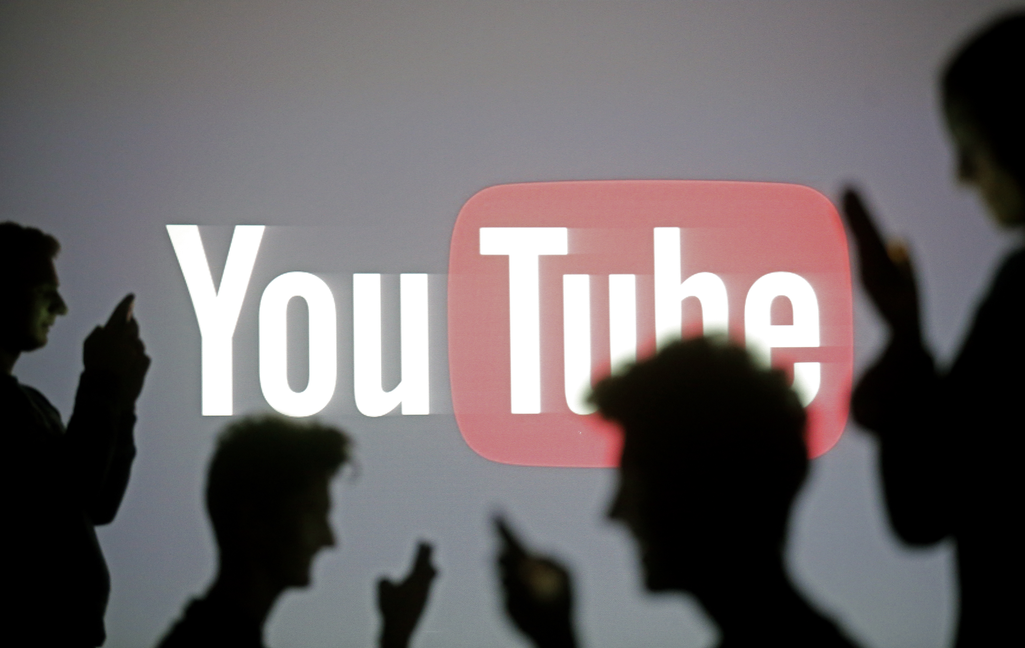 People pose with mobile devices in front of projection of Youtube logo in this picture illustration taken in Zenica