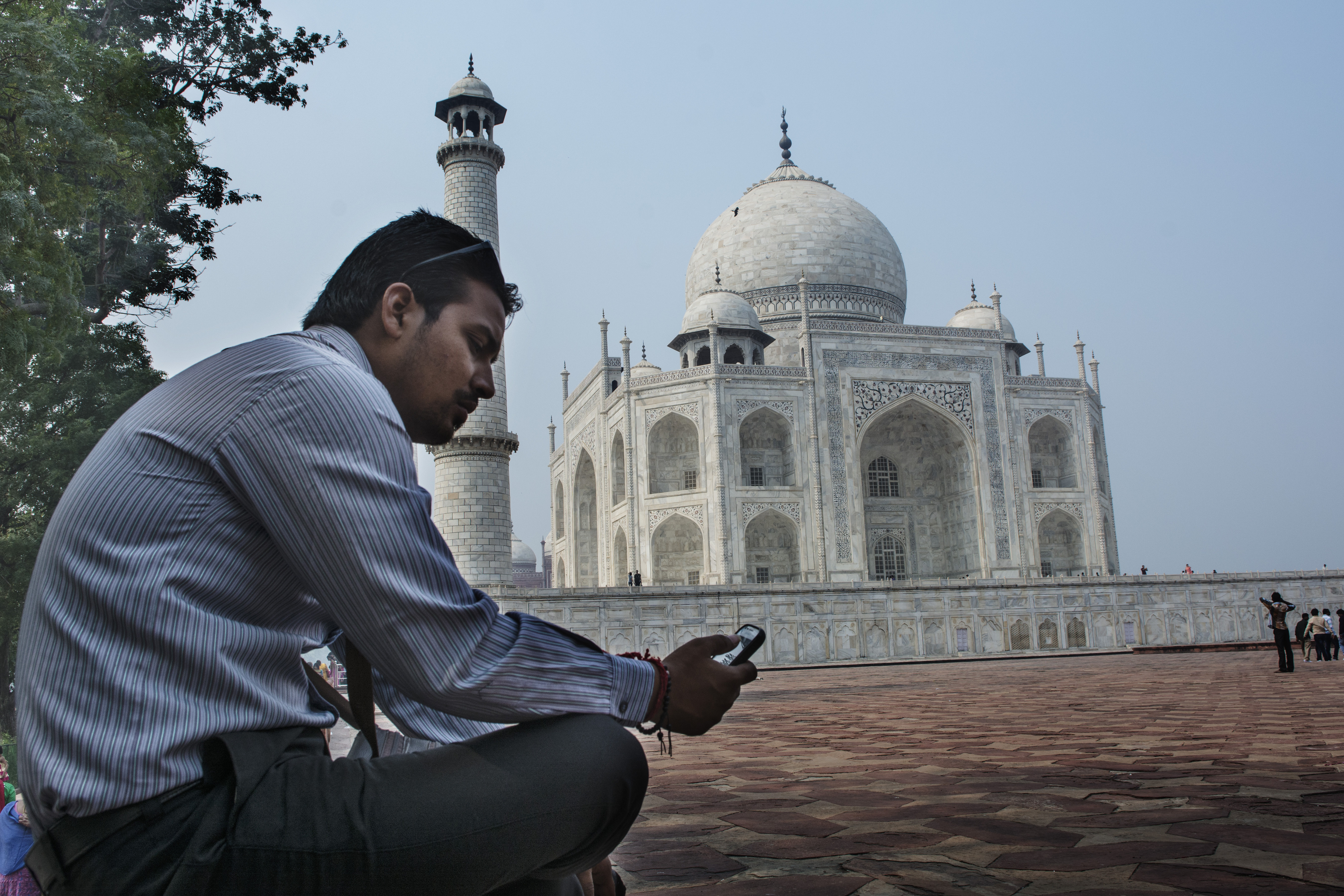 A man checks his cell phone in front of the Taj Mahal. The