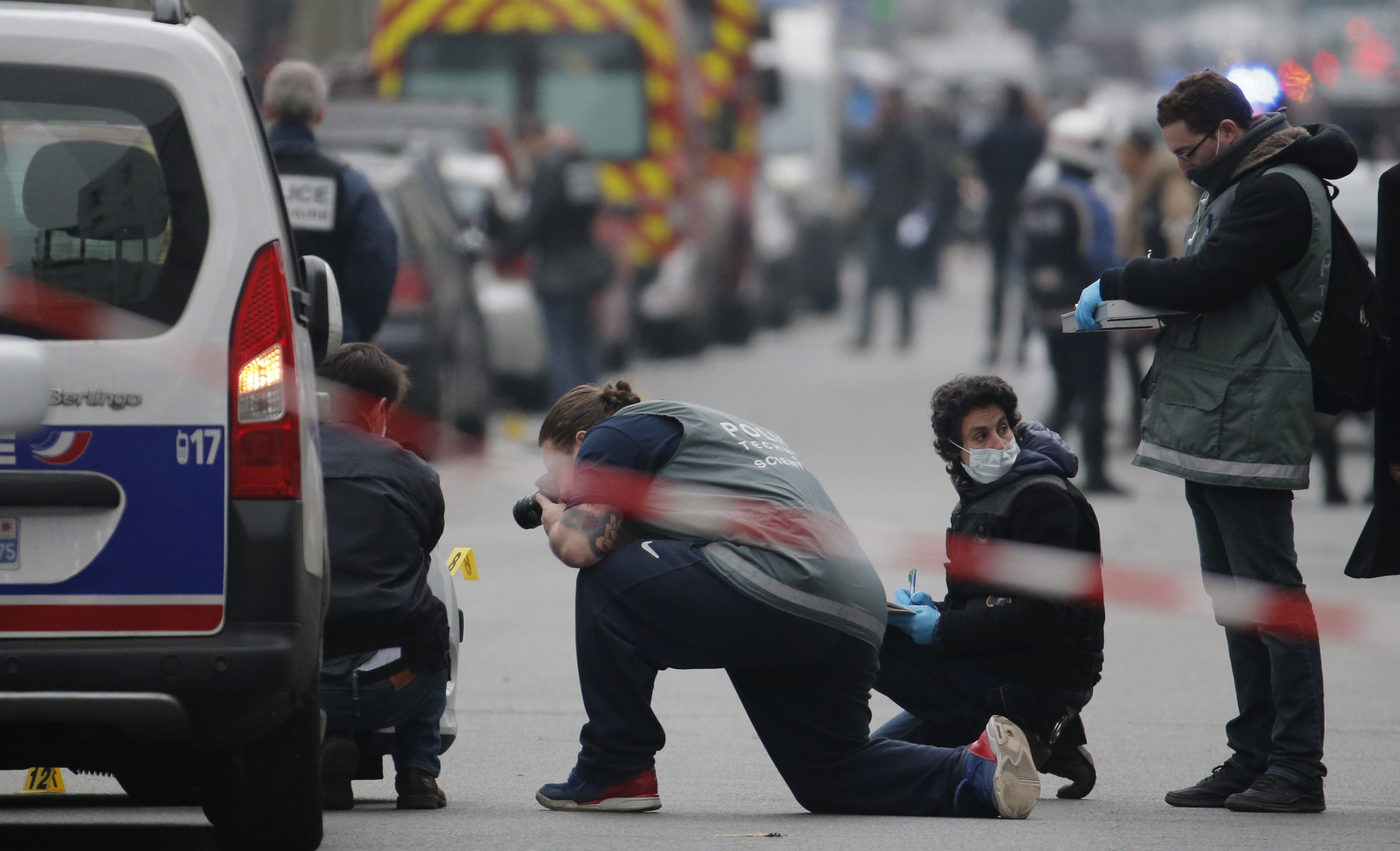 Police investigators examine the impacts from machine gun fire on the front of a police vehicle in the street near the Paris offices of Charlie Hebdo