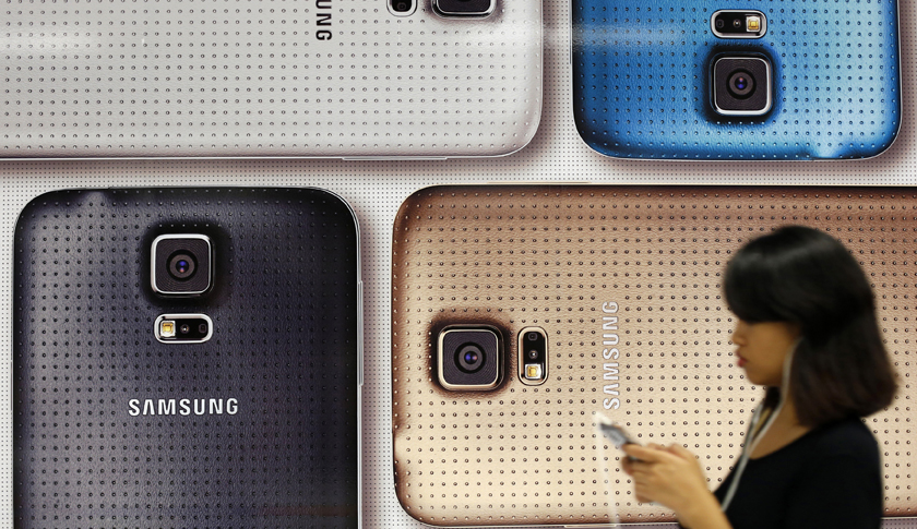 A commuter uses her mobile phone as she walks past a Samsung Galaxy mobile phone advertisement in Singapore