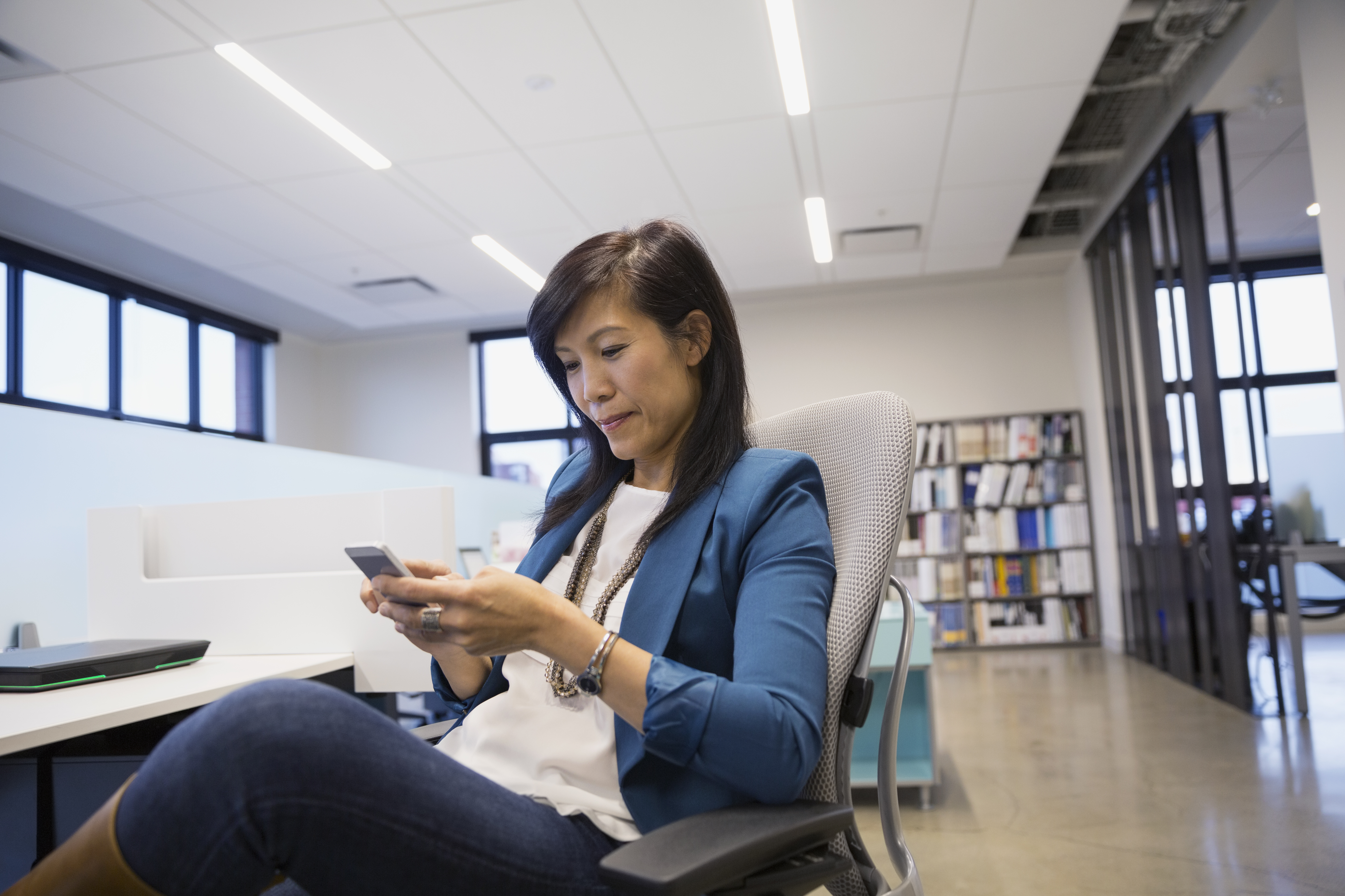 Businesswoman texting on cell phone at office desk