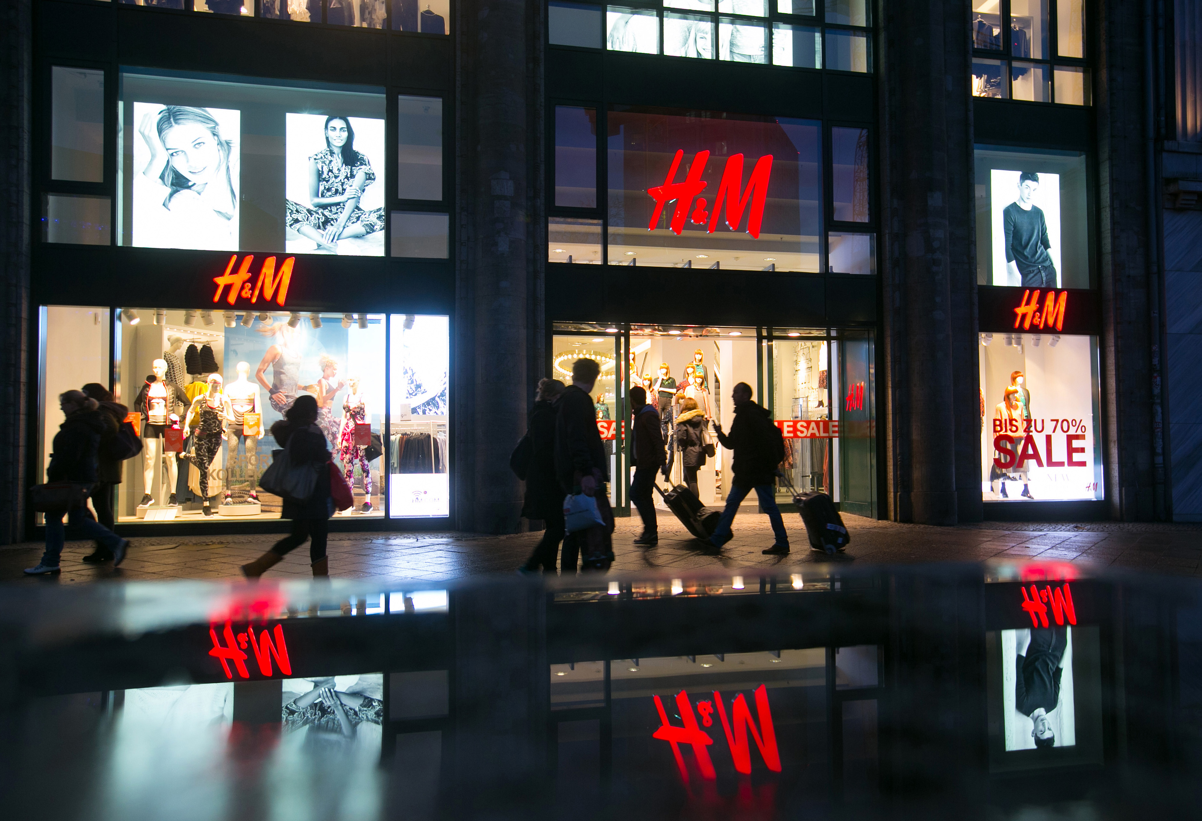 Pedestrians pass an illuminated Hennes & Mauritz AB (H&M) clothing fashion store in Berlin, Germany, on Wednesday, Jan. 7, 2014. As European Central Bank policy makers gather for their first meeting of 2015 today, the backdrop is a 0.2 percent annual drop in consumer prices, the first in more than five years. Photographer: Krisztian Bocsi/Bloomberg