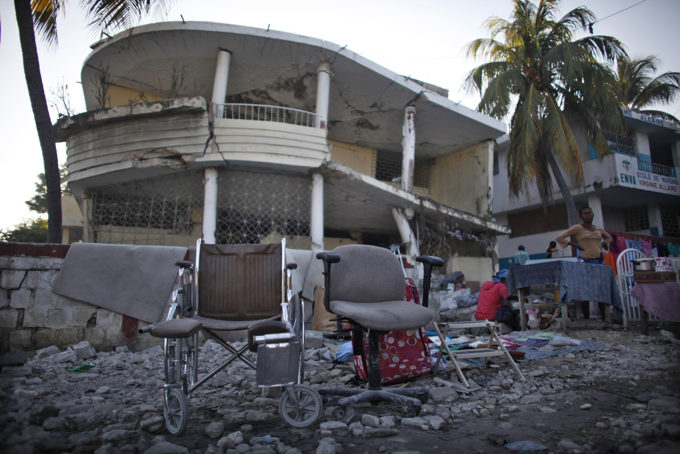 A wheelchair and other items are displayed to sell in front of a destroyed building by the January 2010 earthquake in Port-au-Prince