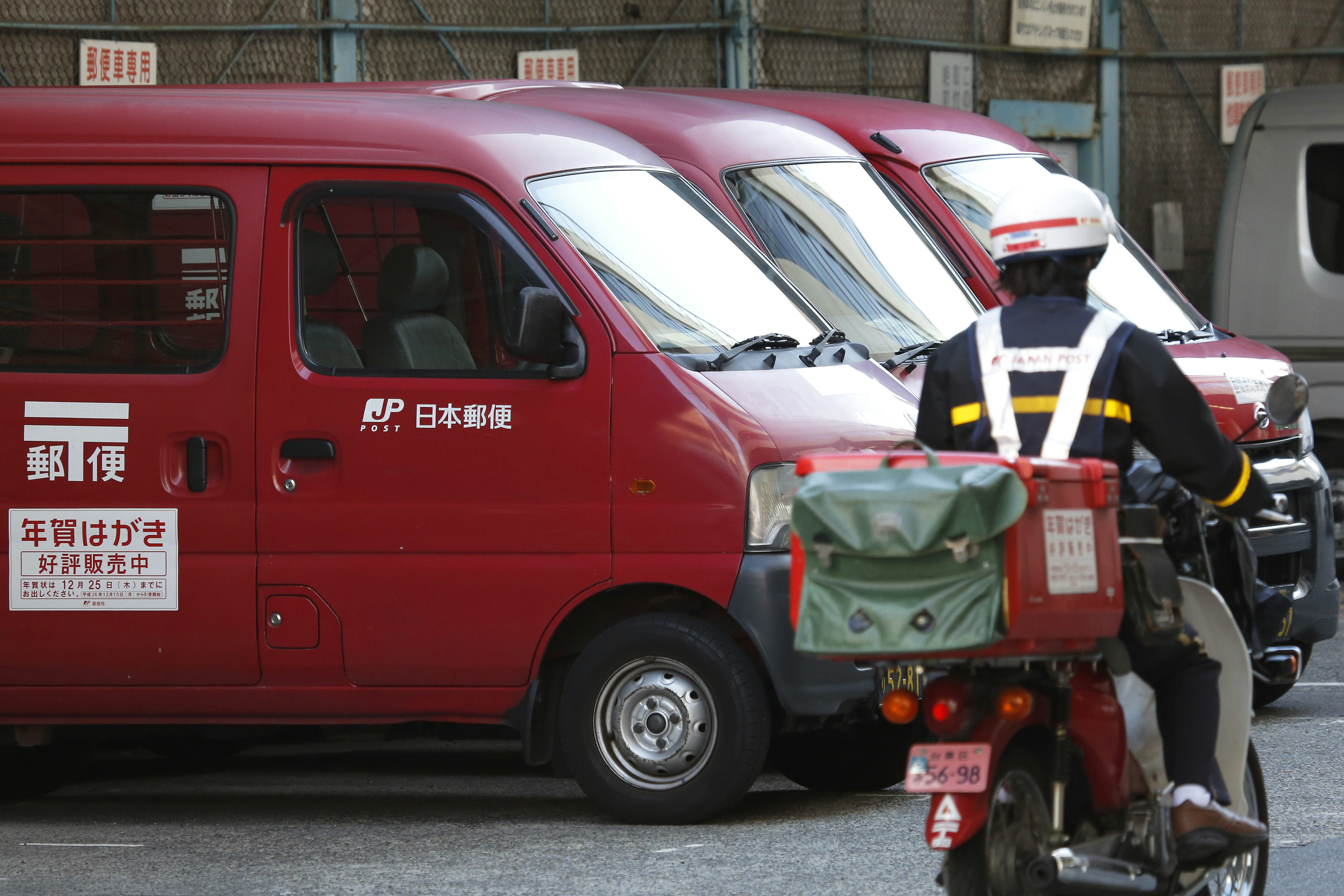 Japan Post vans sit parked while an employee drives a motorcycle into the company's branch in Tokyo, Japan