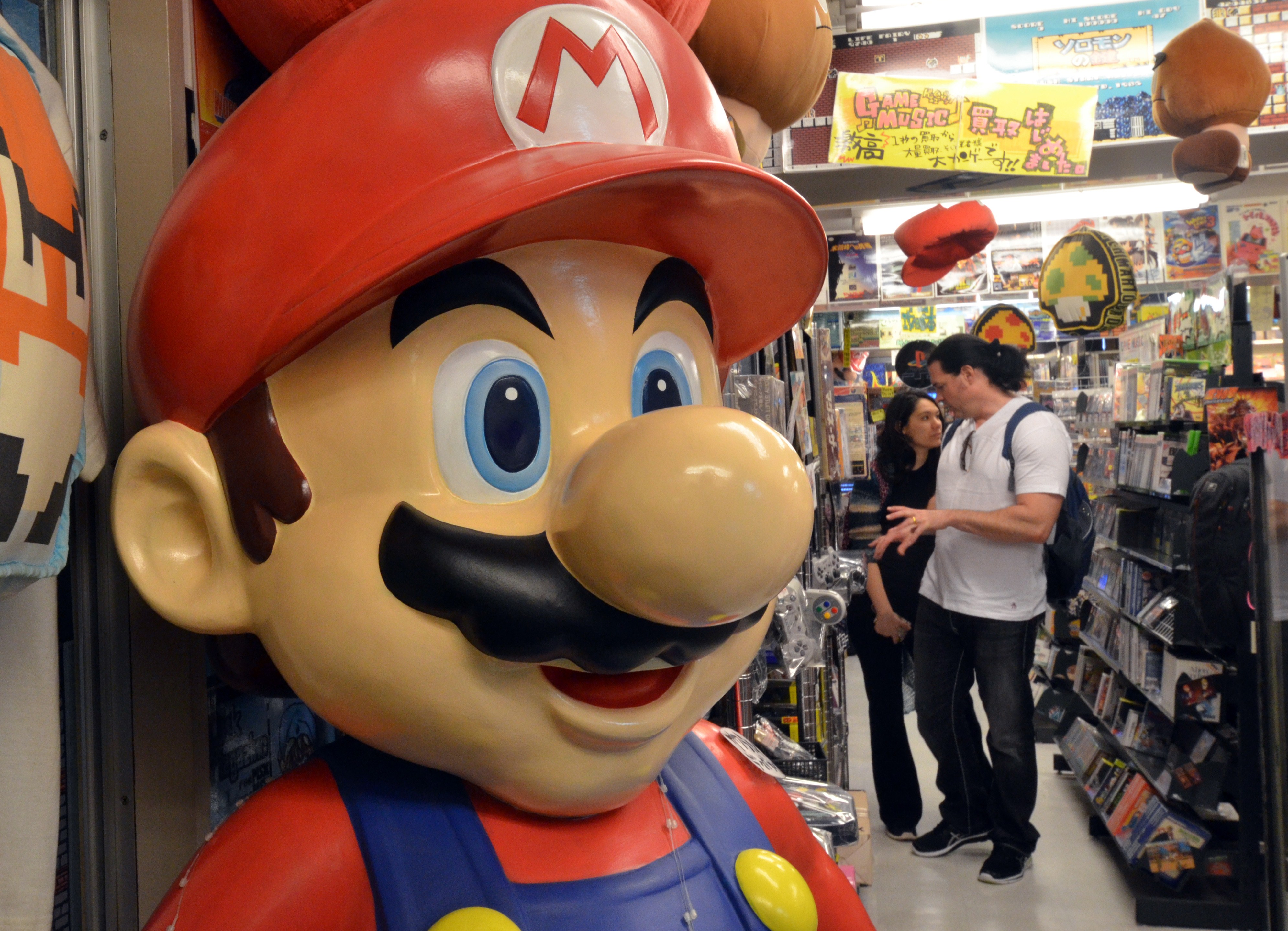 Customers check videogame consoles and softwares at a shop in Tokyo, while a large figure of Nintendo's character Super Mario stands nearby.