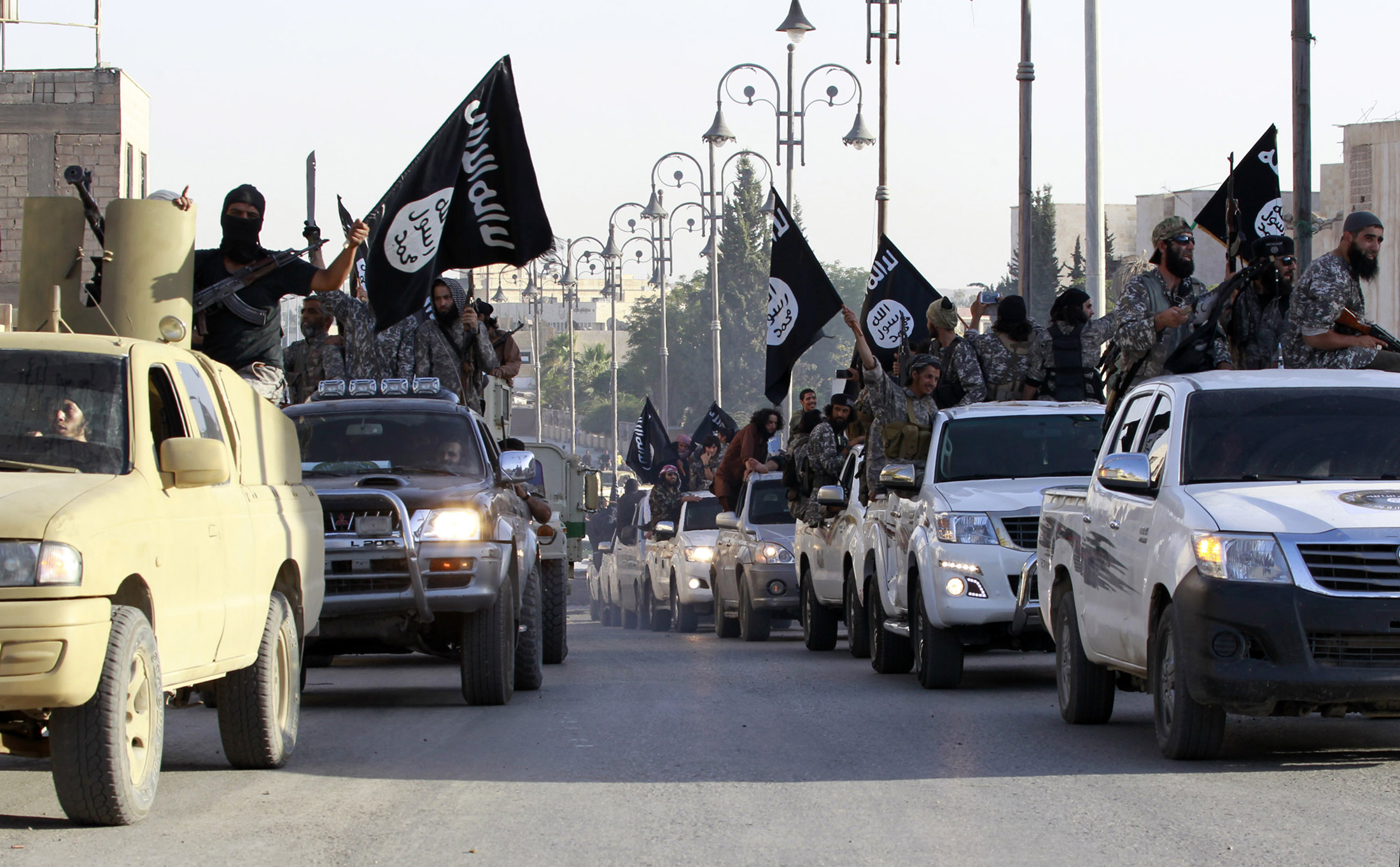 Militant Islamist fighters parade on military vehicles along the streets of northern Raqqa province