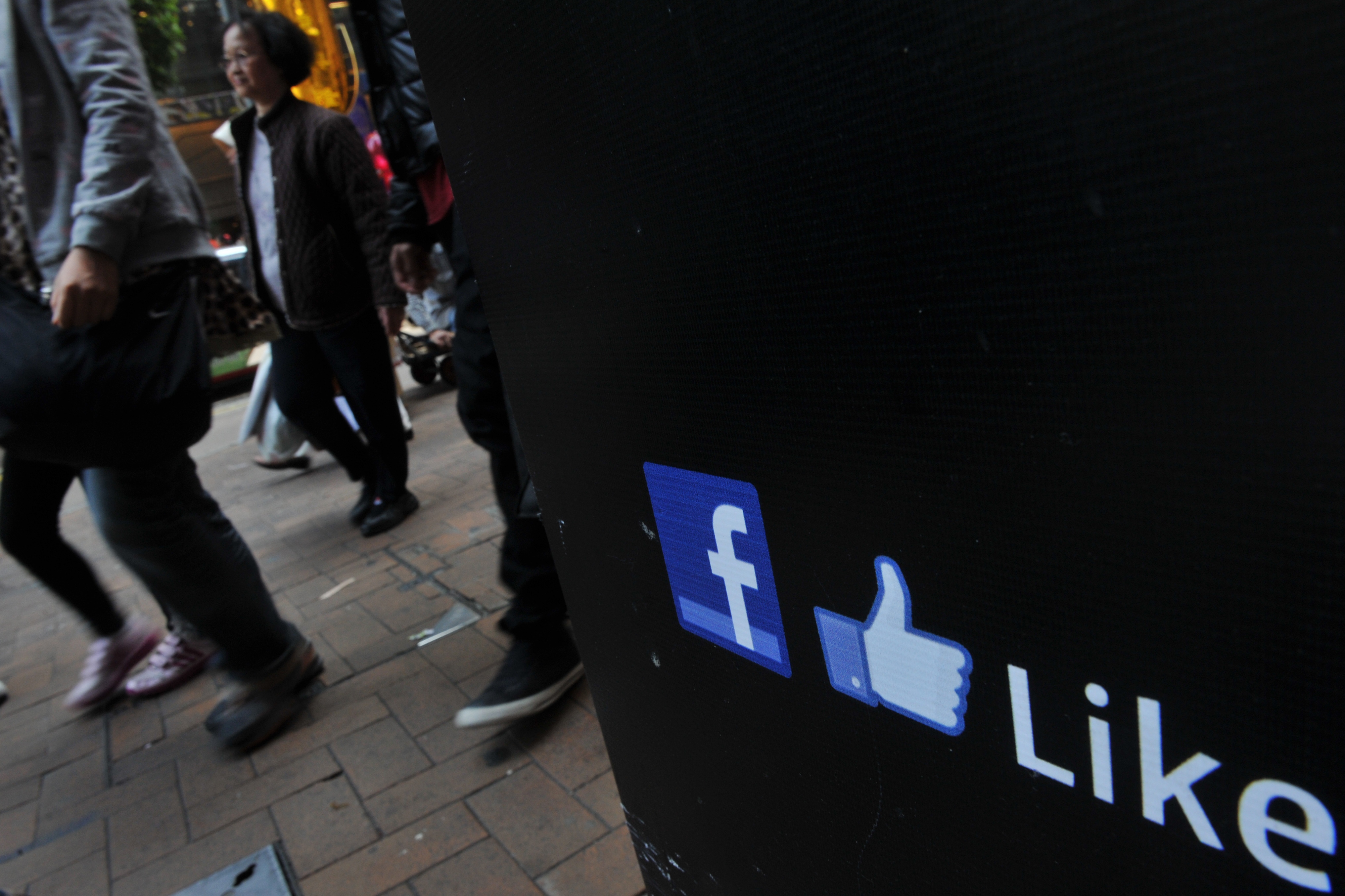 People walk by a Facebook logo and a thu