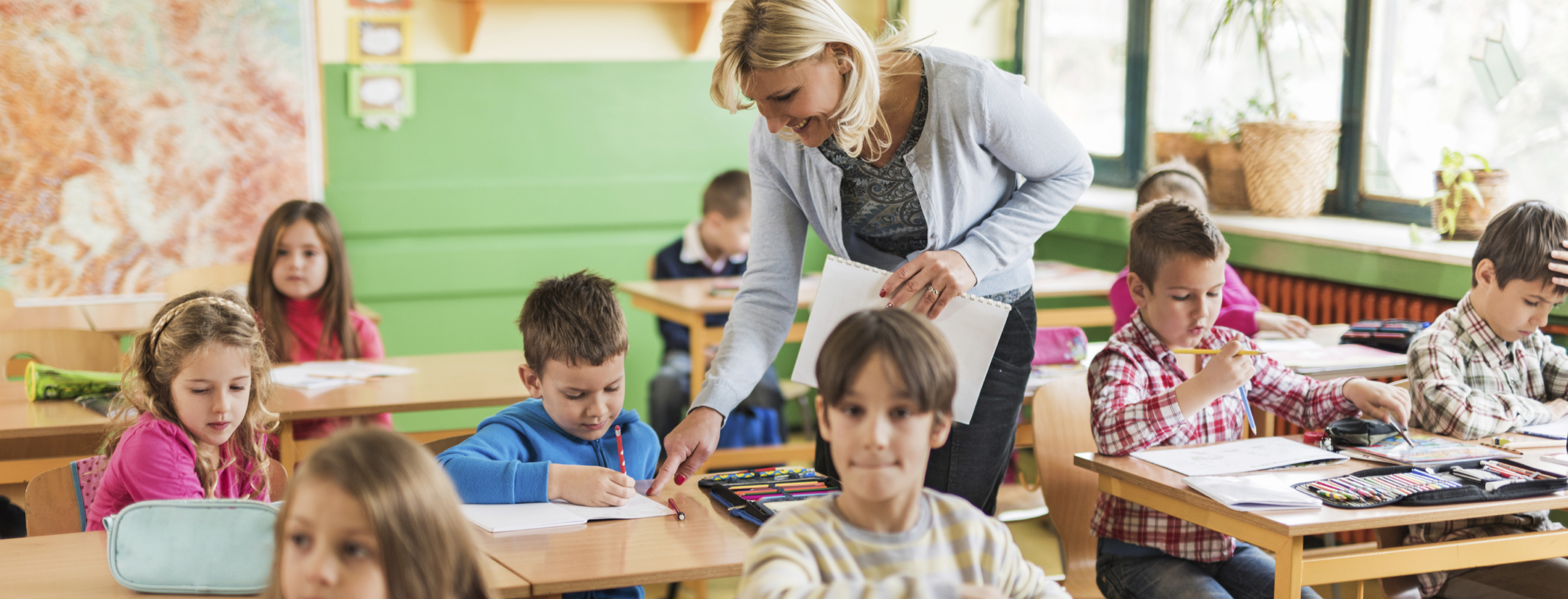 Happy female teacher assisting elementary students in the classroom.