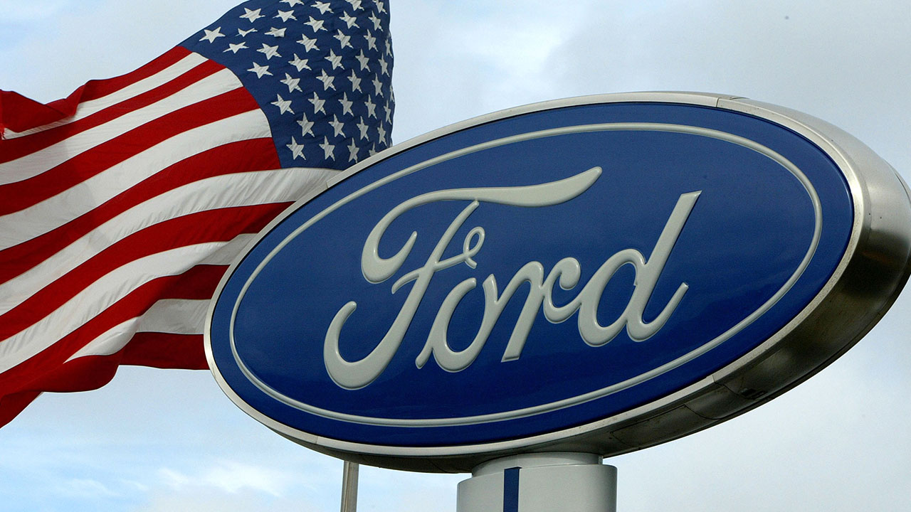 SAN BRUNO, CA - JANUARY 26: An American flag waves behind a Ford sign at a Ford dealership January 26, 2004 in San Bruno, California. Toyota Motor Corp. surpassed Ford Motor Co. of the United States as the world's No. 2 automaker, according to global sales numbers released today by the Japanese automaker that confirmed last week's preliminary data. (Photo by Justin Sullivan/Getty Images)