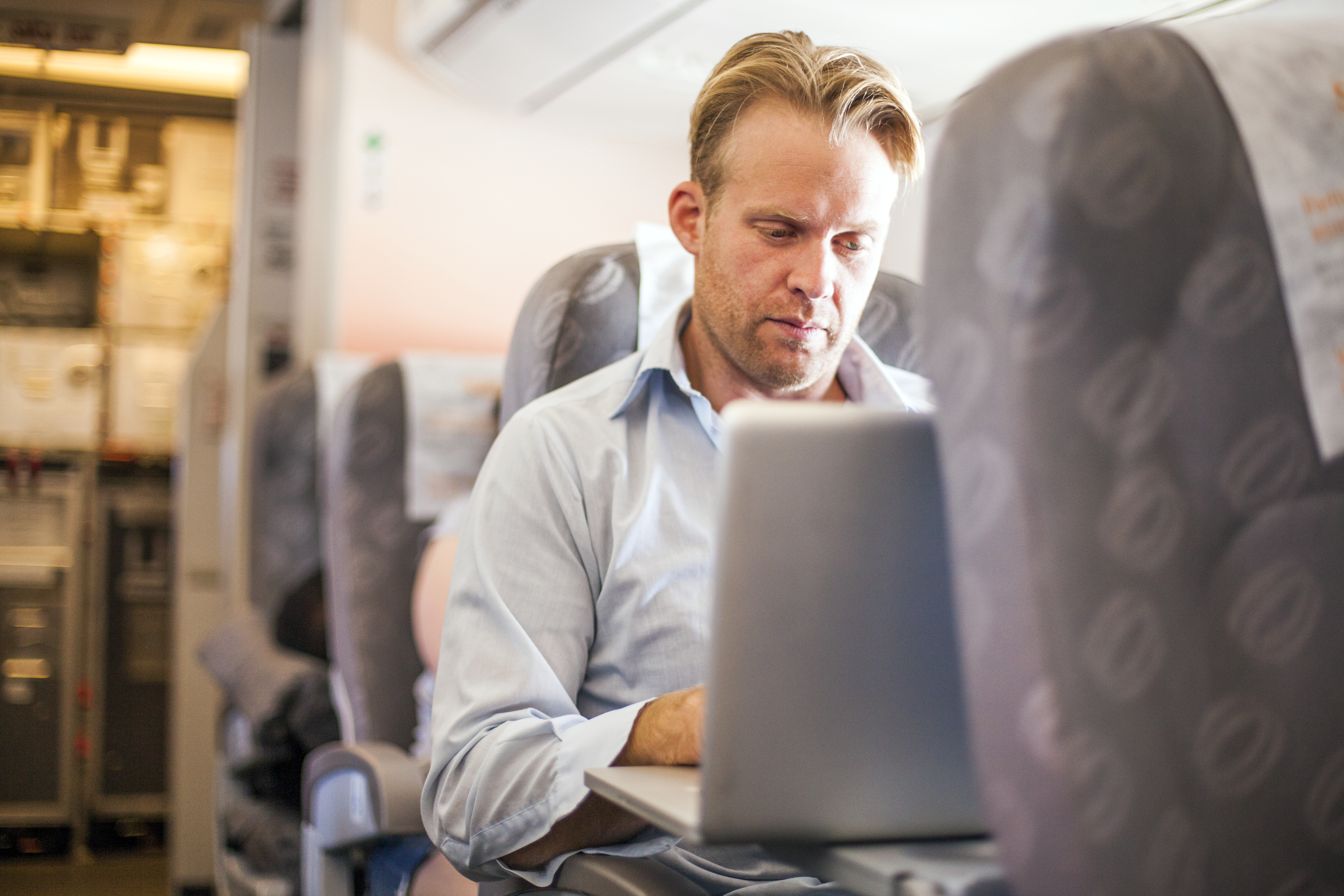 A businessman working on a lap top computer in an airplane.