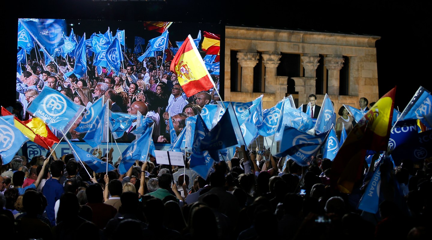 Supporters wave flags as People's Party (PP) leader Mariano Rajoy delivers a speech during a rally at the start of the official campaign period for Spain's general election in Madrid