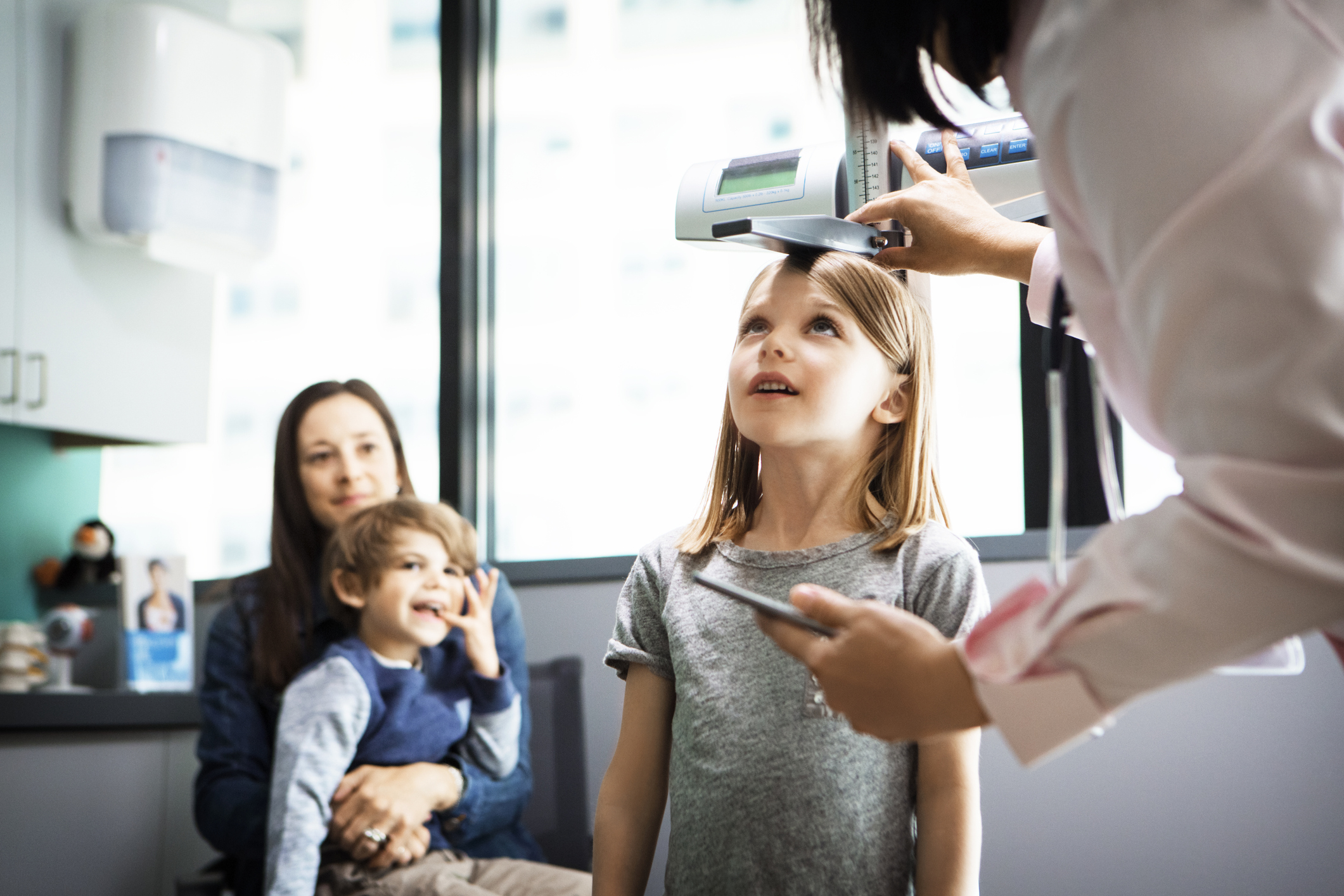 Doctor measuring girls height while family sitting at clinic