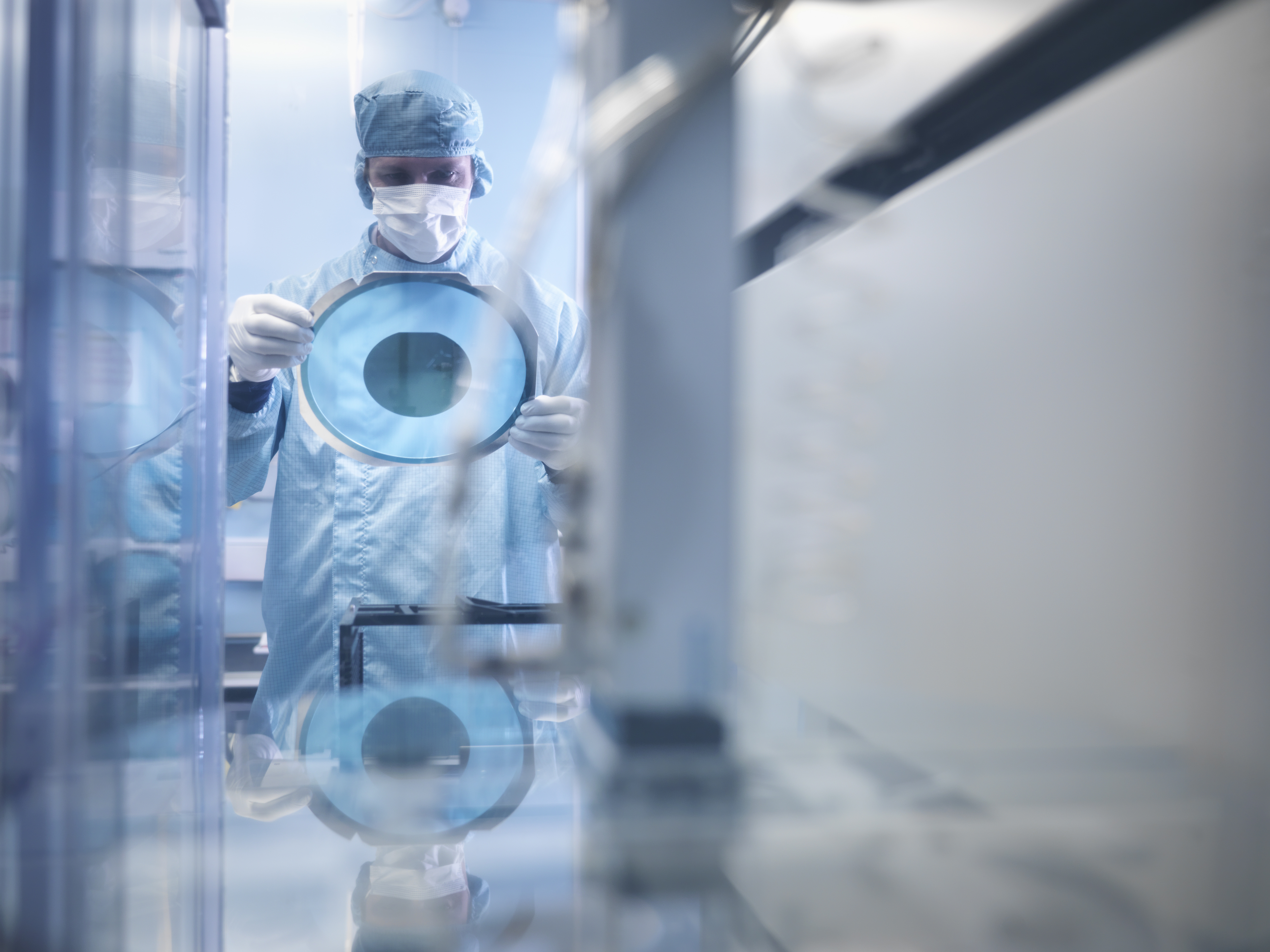 Electronics worker holding silicon wafer by cutting machine in clean room