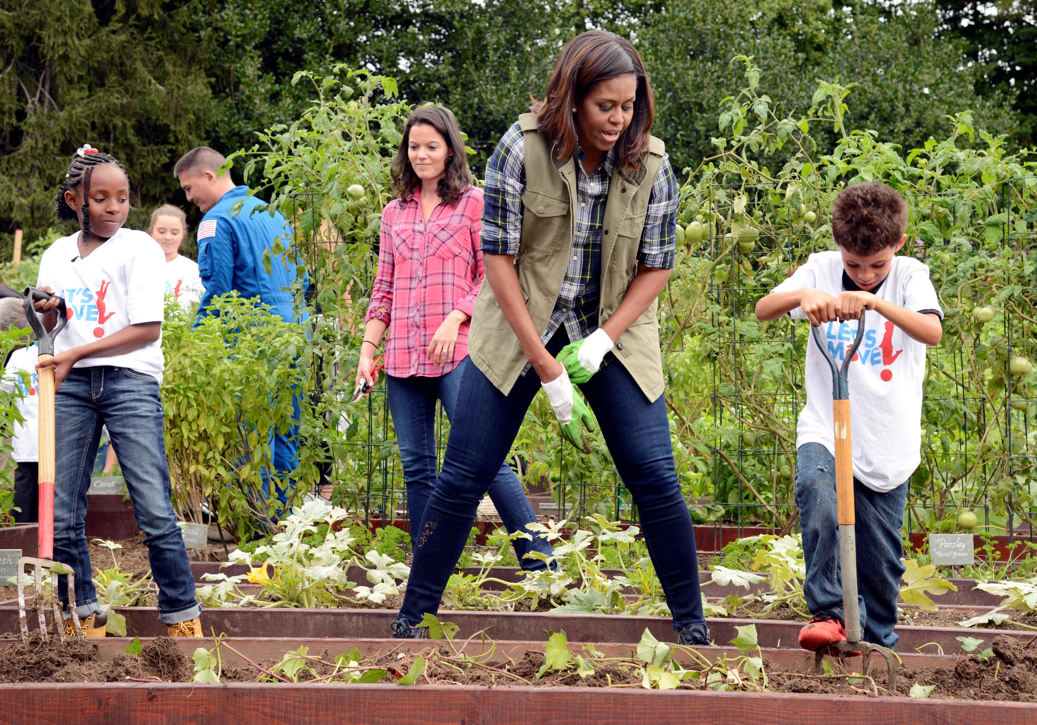 First Lady Michelle Obama encourages a youngster with a pitchfork as they harvest vegetables in the White House Kitchen Garden in Washington