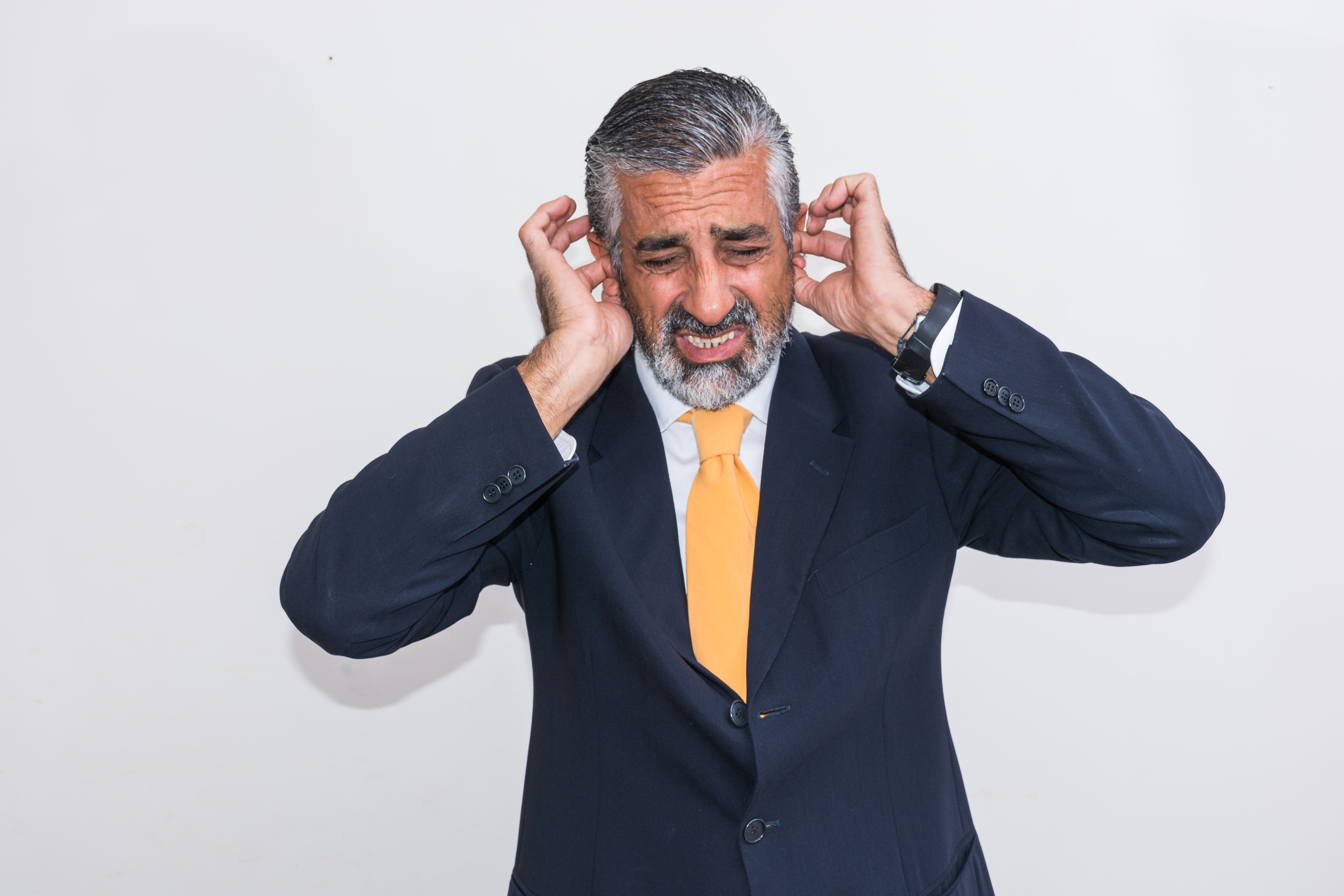 Businessman With Hands Covering Ears Against Wall