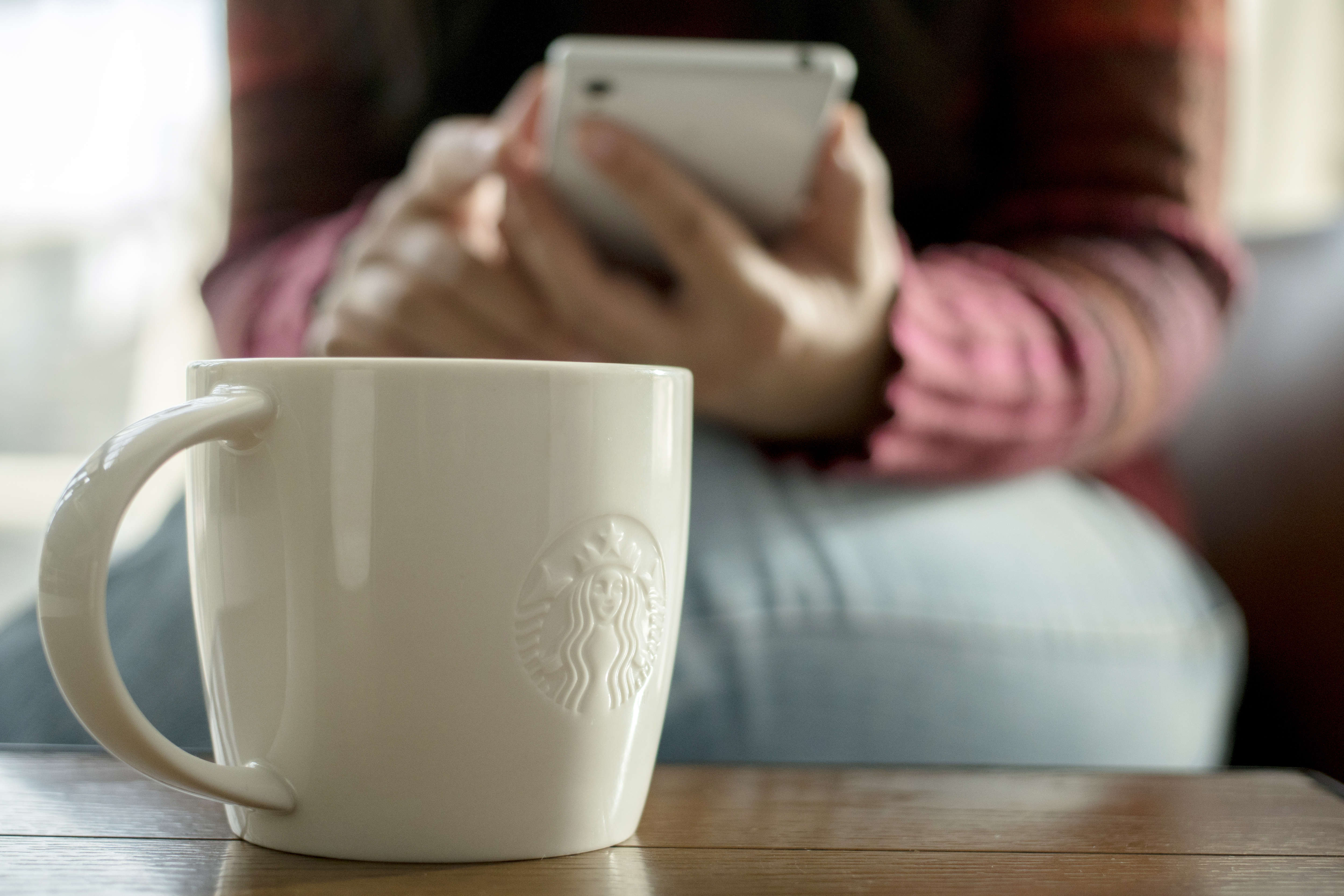 A Starbucks coffee cup on table, beside which a customer is