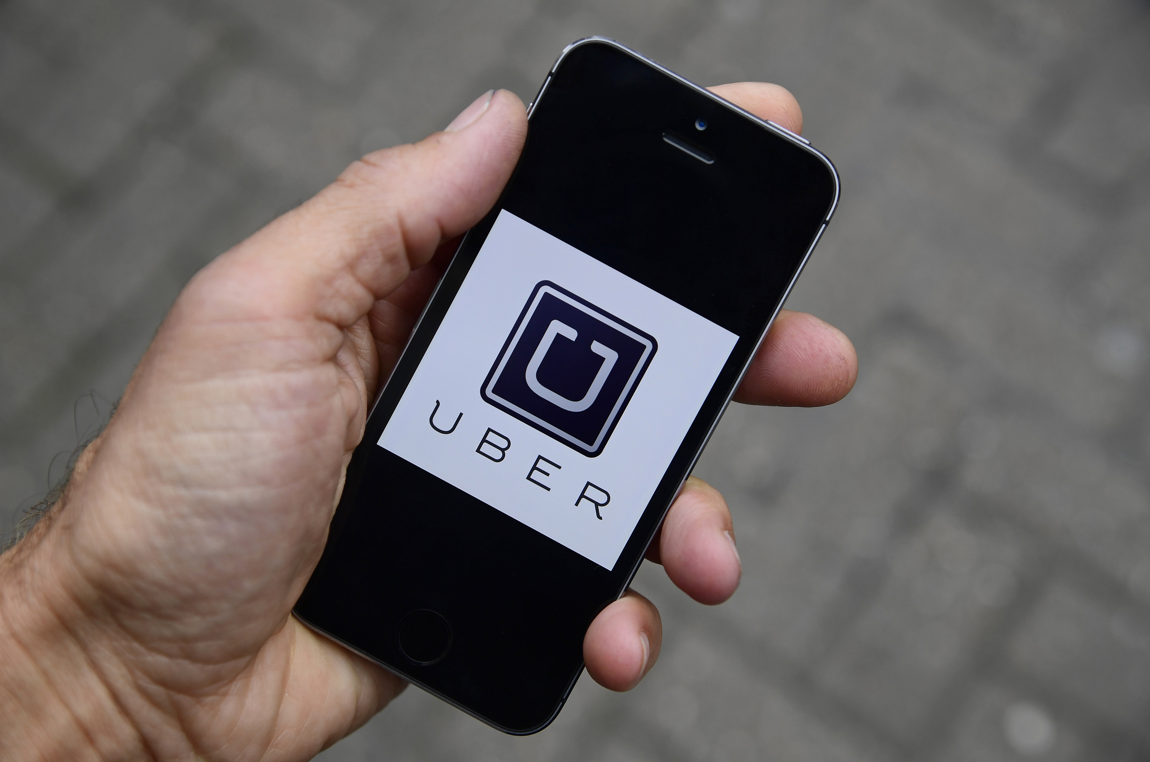 A photo illustration shows the Uber app logo displayed on a mobile telephone, as it is held up for a posed photograph in central London