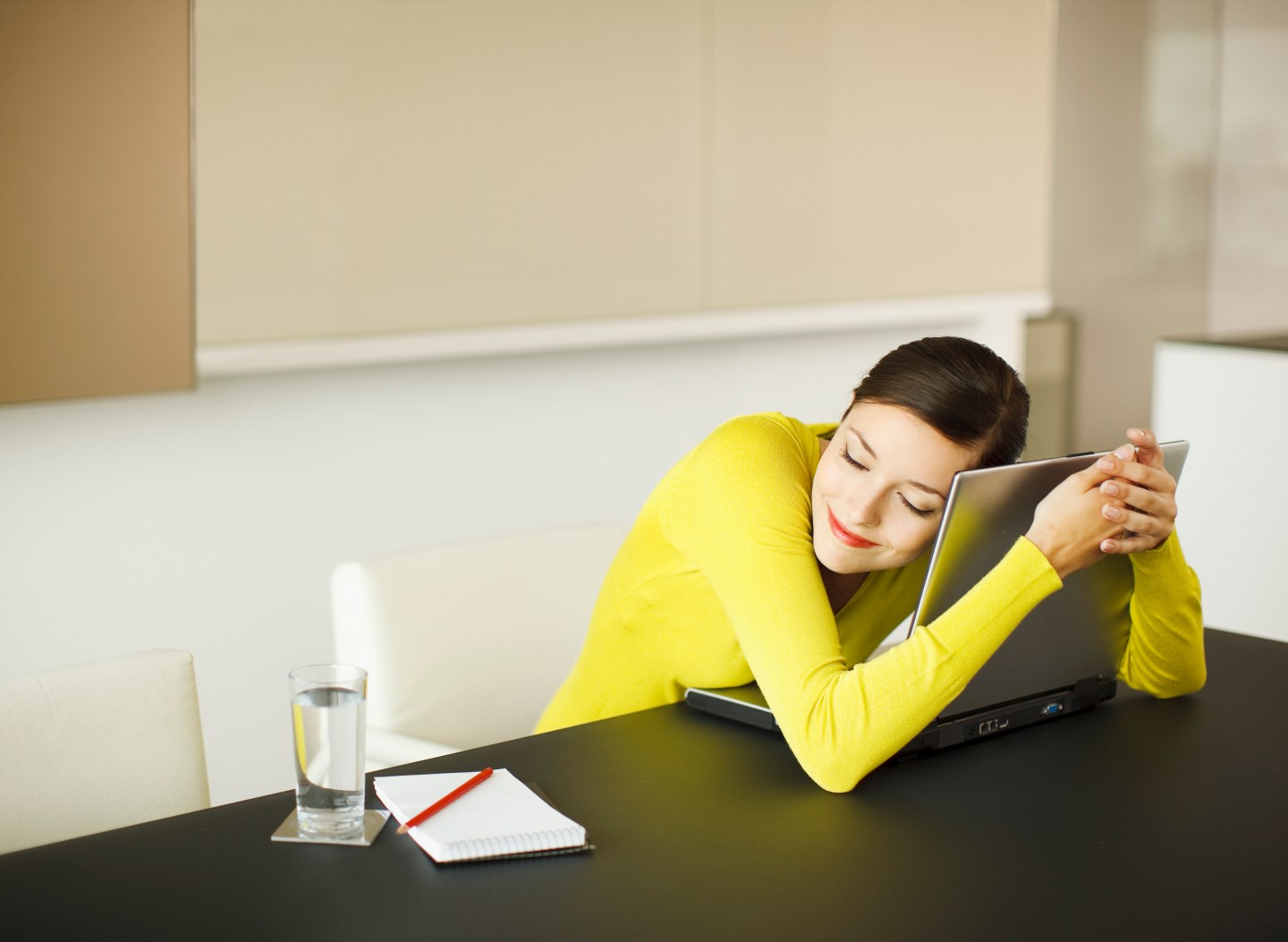 Smiling businesswoman hugging laptop in conference room