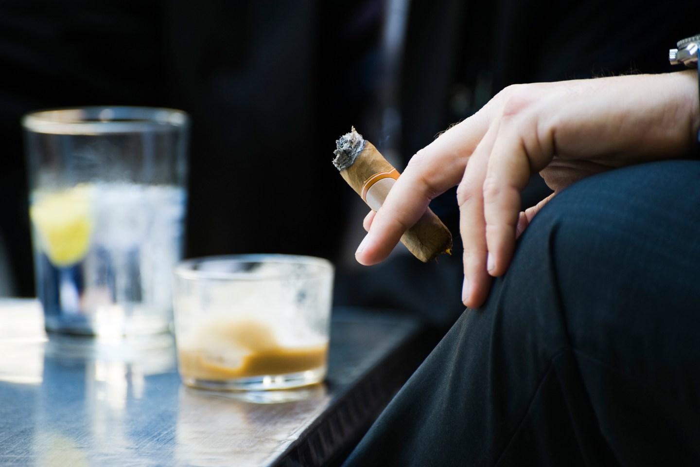 Man's hand on knee holding smoking cigar, close-up