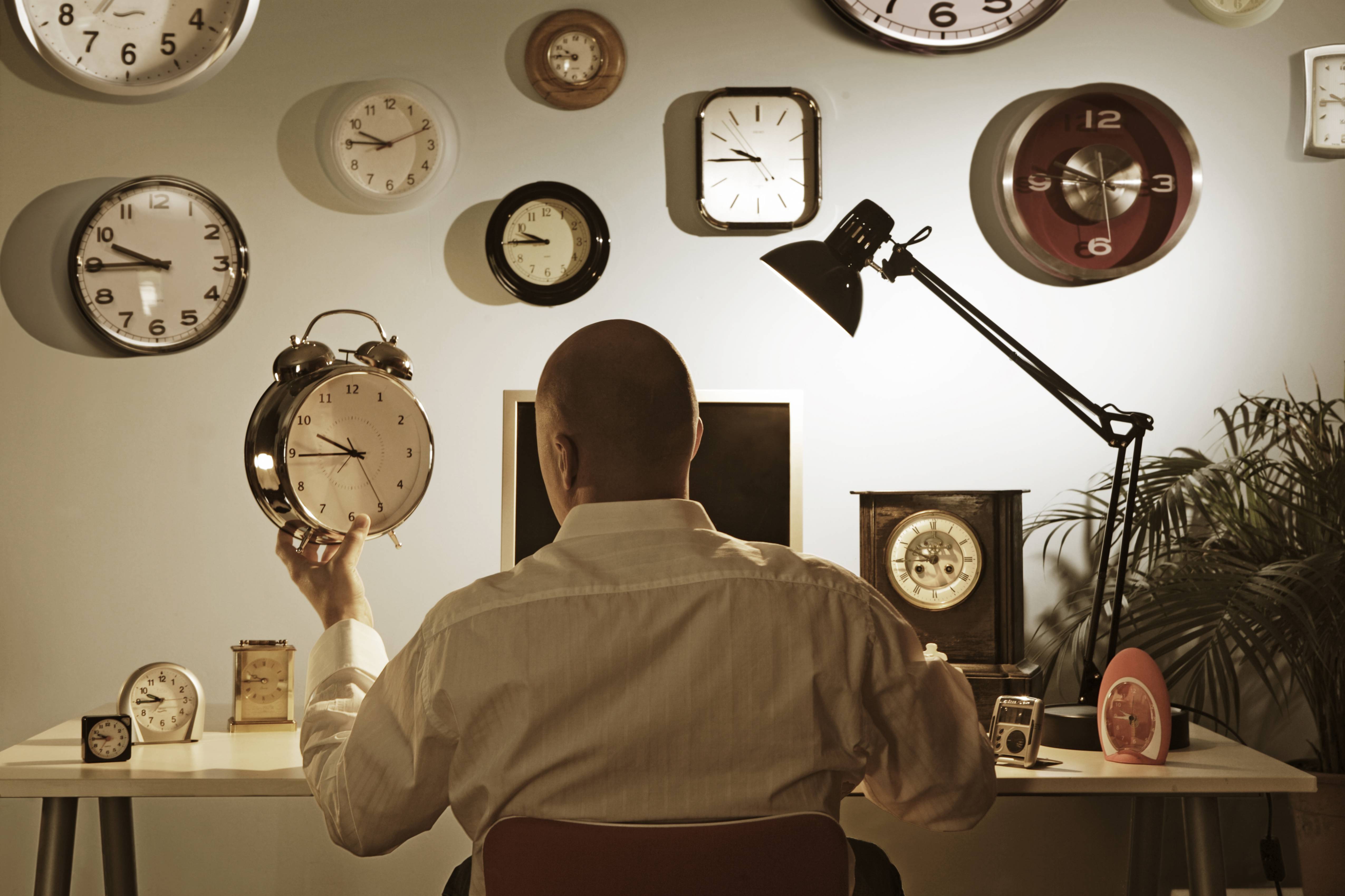 man sitting at desk surrounded by clocks