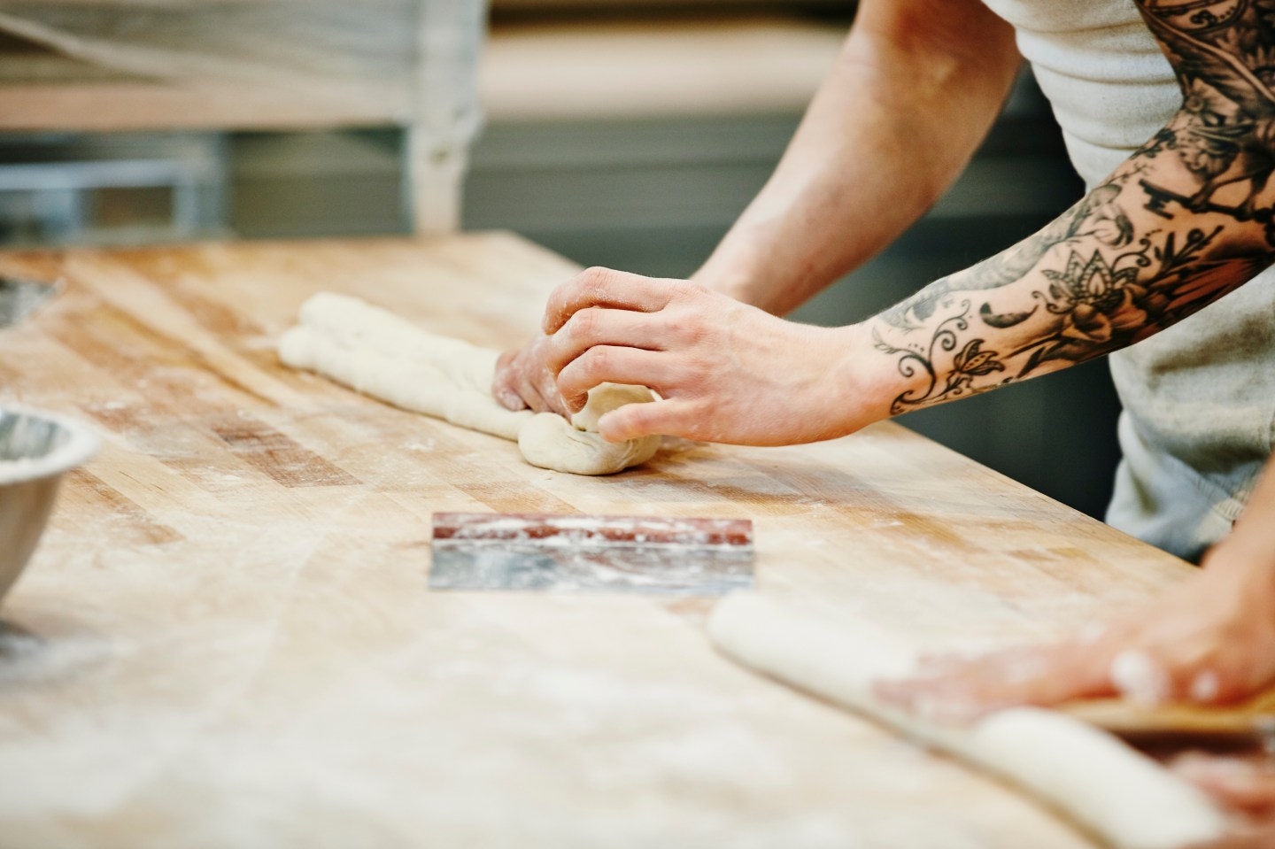 Bakers shaping dough for baguettes at table in bakery