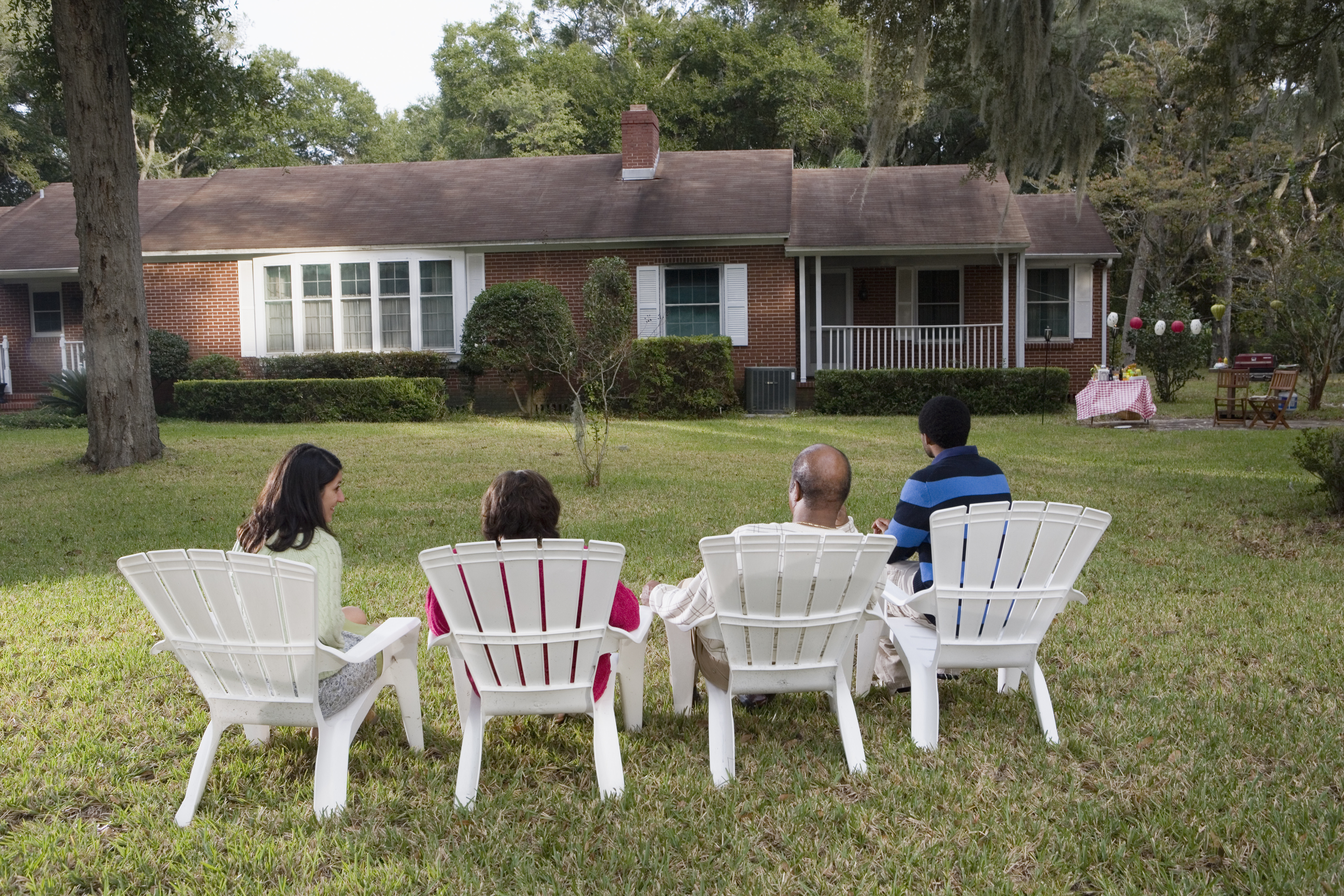Rear view of four people in lawn chairs in backyard