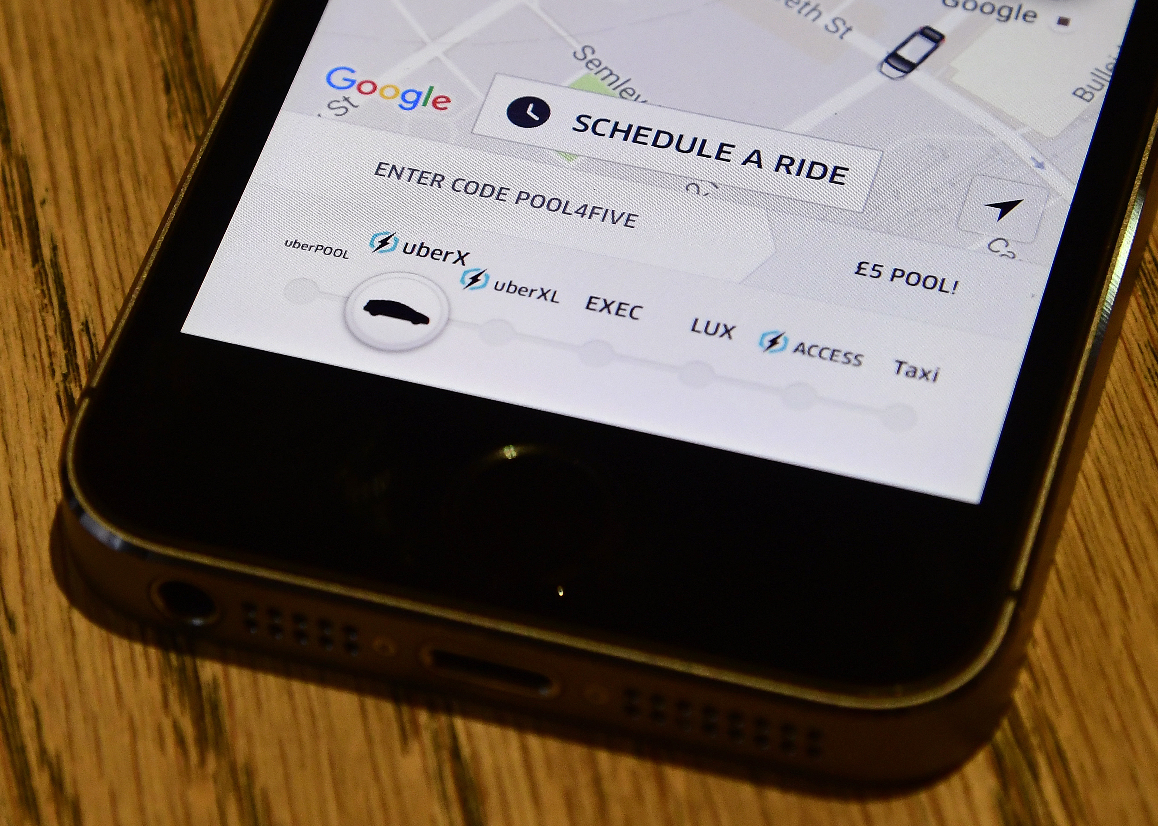 A photo illustration shows the Uber app logo displayed on a mobile telephone, as it is held up for a posed photograph in central London