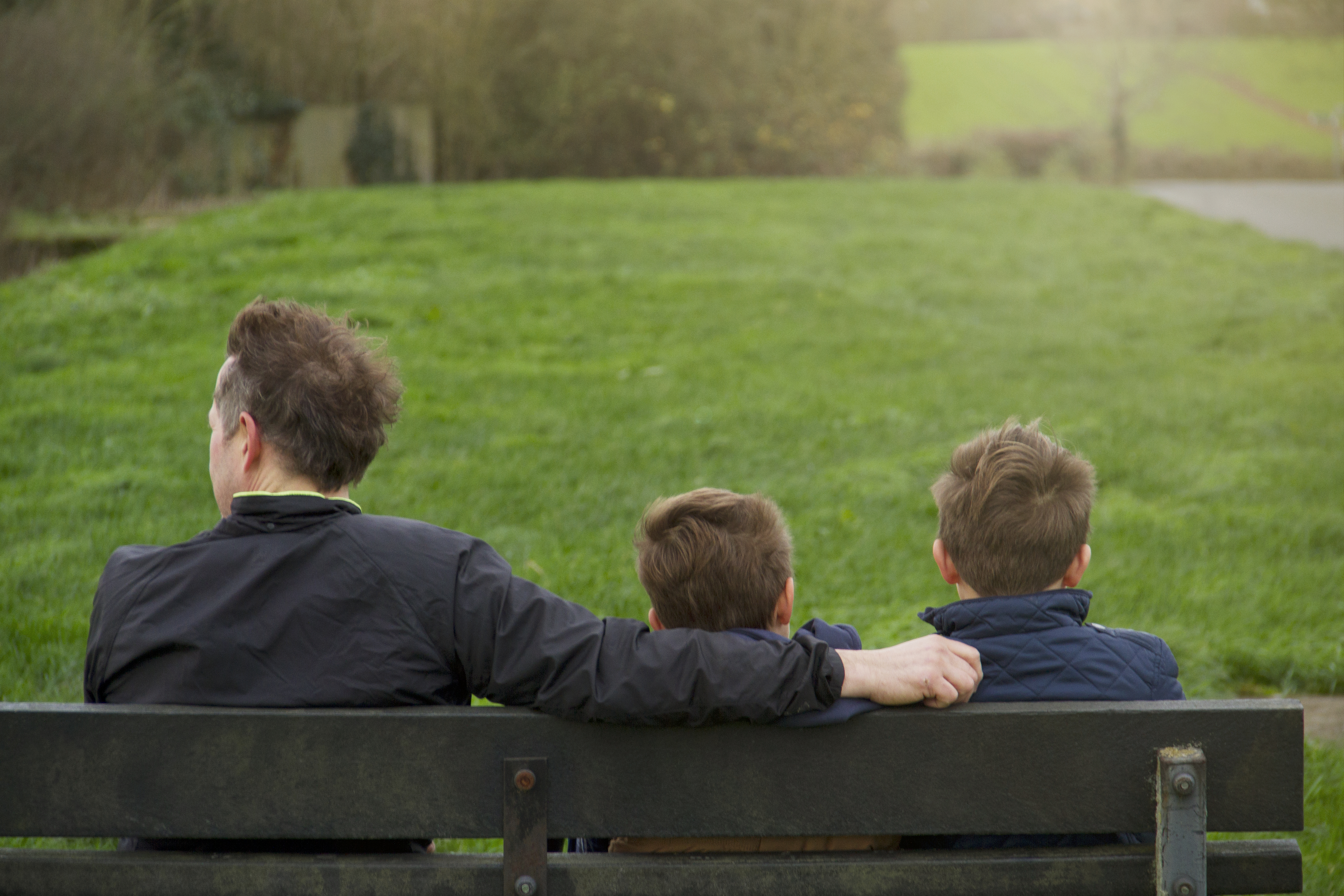 Father And Two Sons Sat On Bench In Countryside