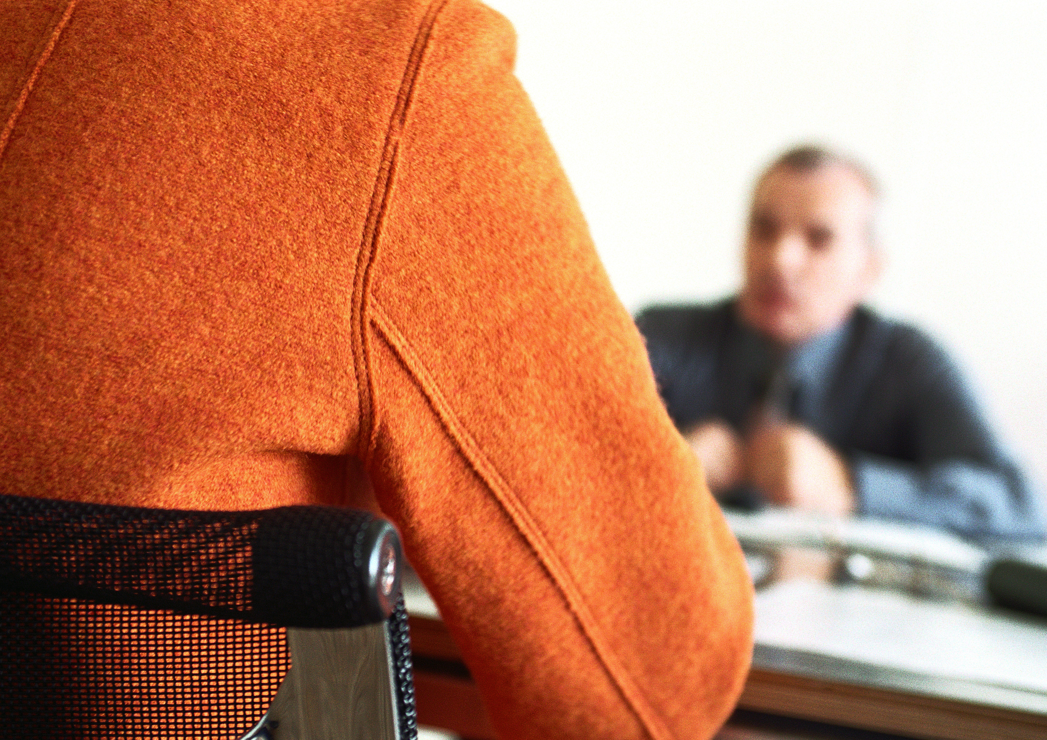 Businessman sitting at table blurred in distance, person's back in foreground.