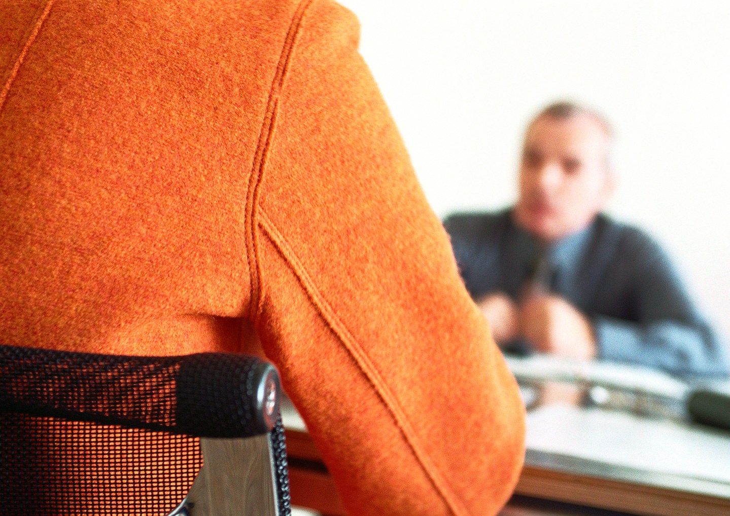 Businessman sitting at table blurred in distance, person's back in foreground.