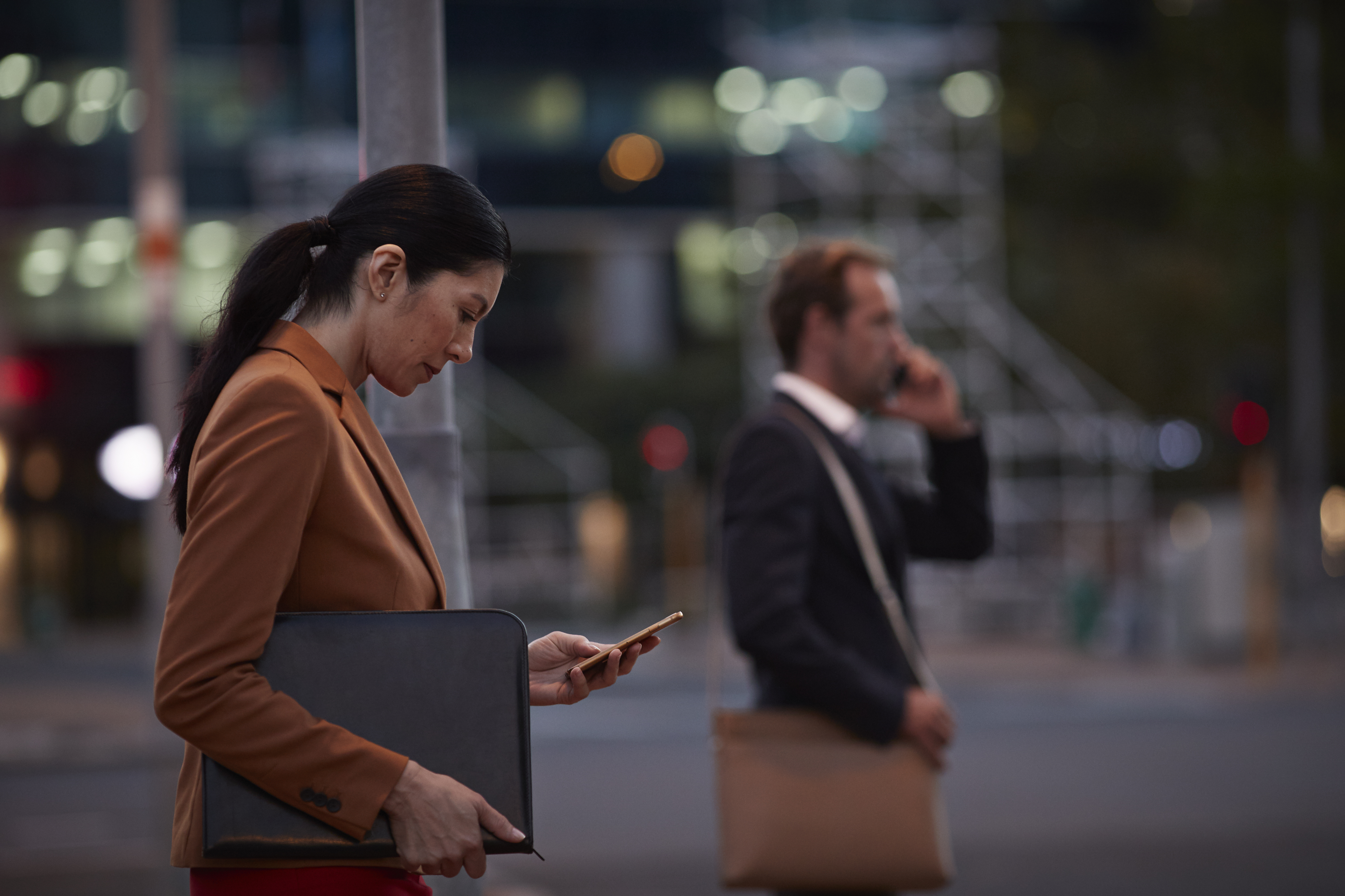 Businesswoman on street looking at phone, at night