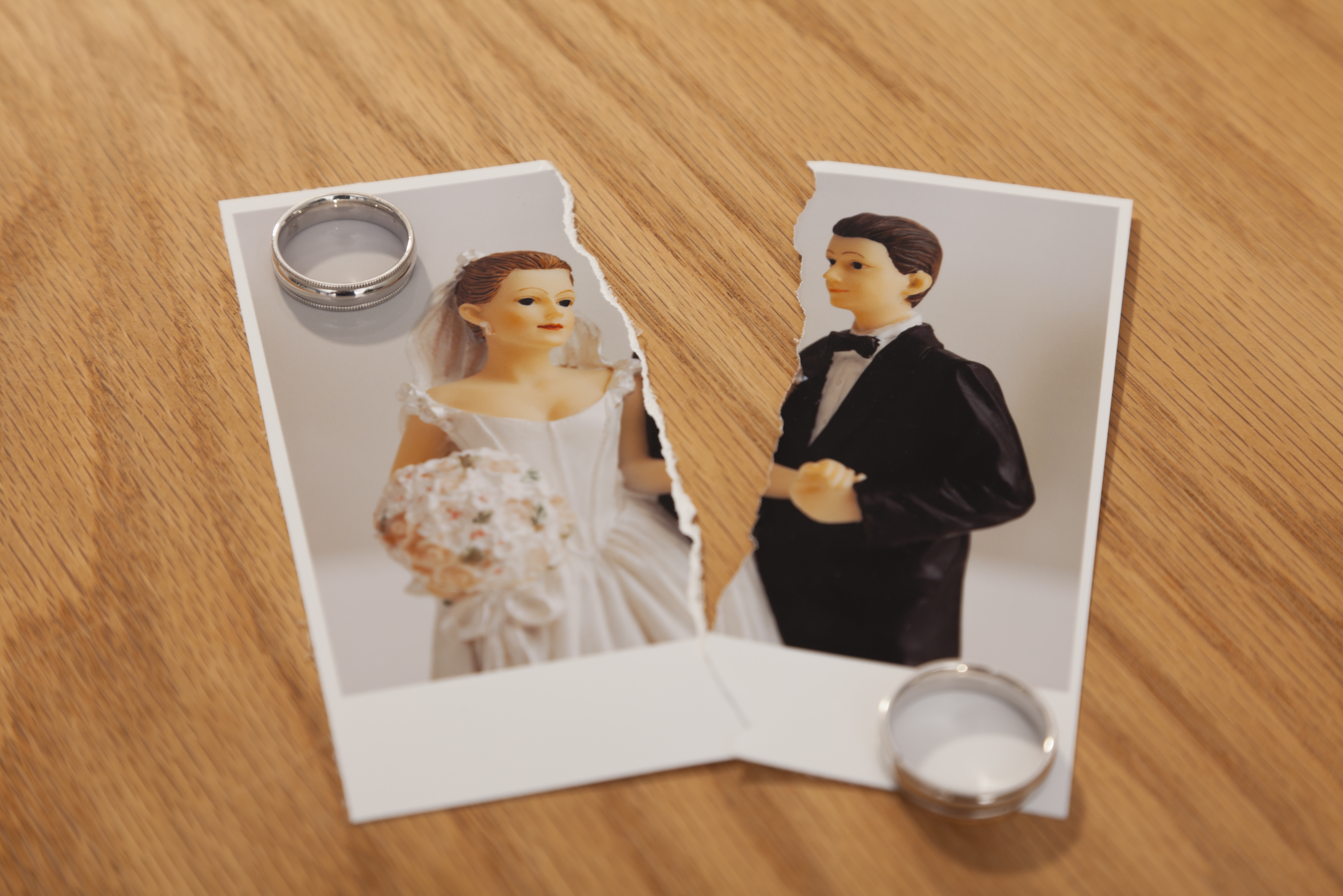 Studio shot of photo of bride and groom figurines torn in half and wedding rings
