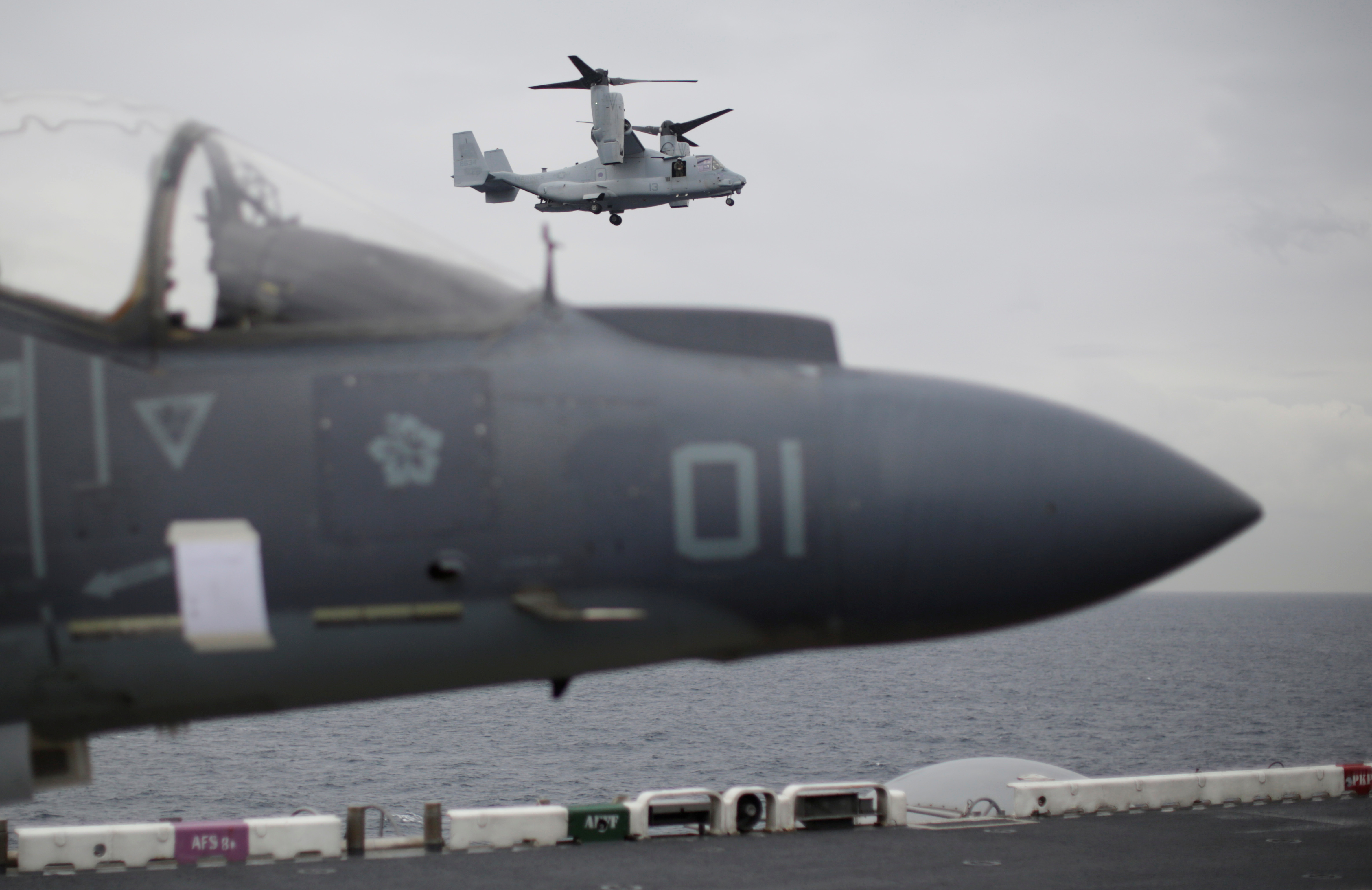 A U.S. Marines MV-22 Osprey Aircraft flies over a jet before landing on the deck of the USS Bonhomme Richard amphibious assault ship off the coast of Sydney