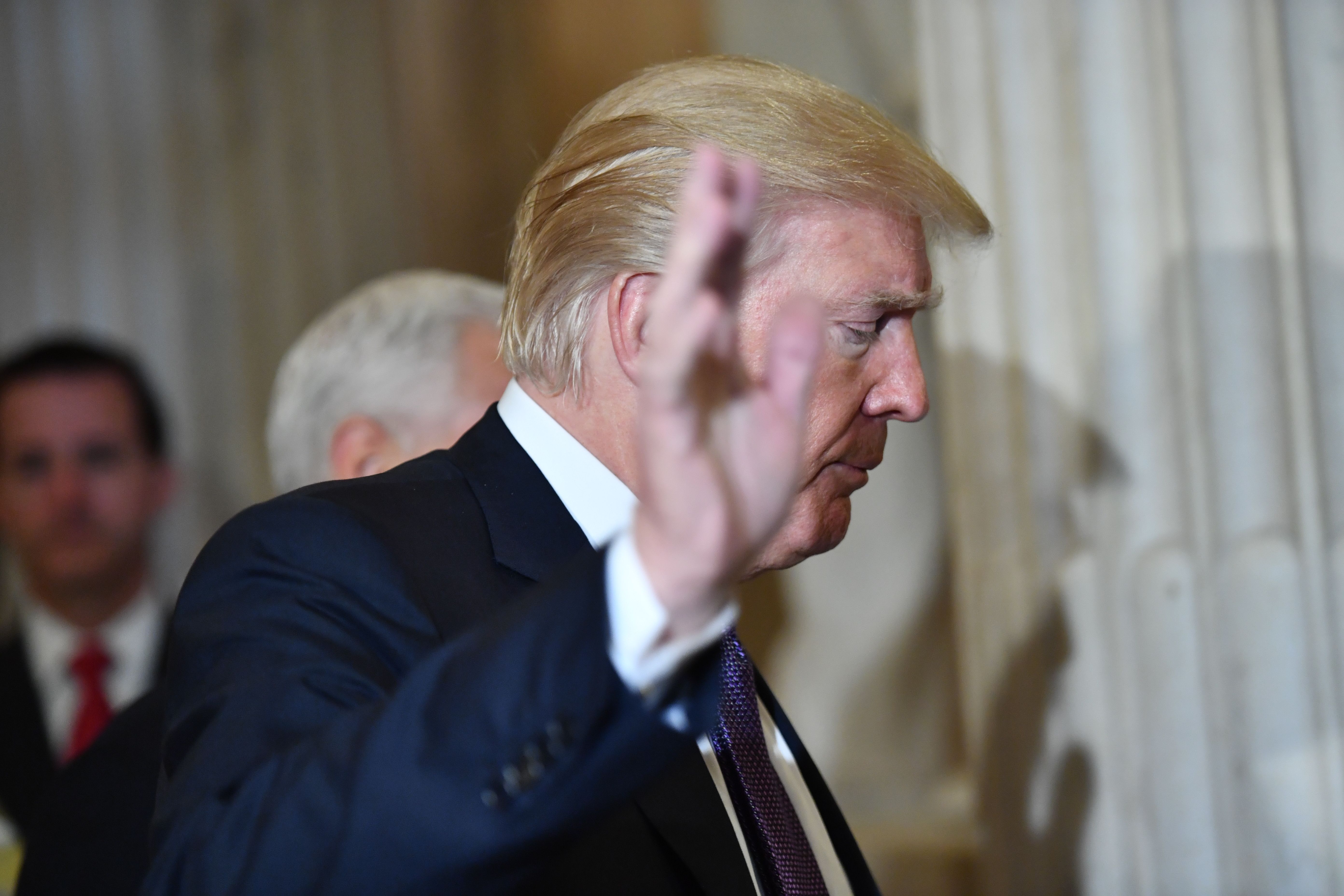 Donald Trump faces right and raises his right hand in a dismissive gesture.