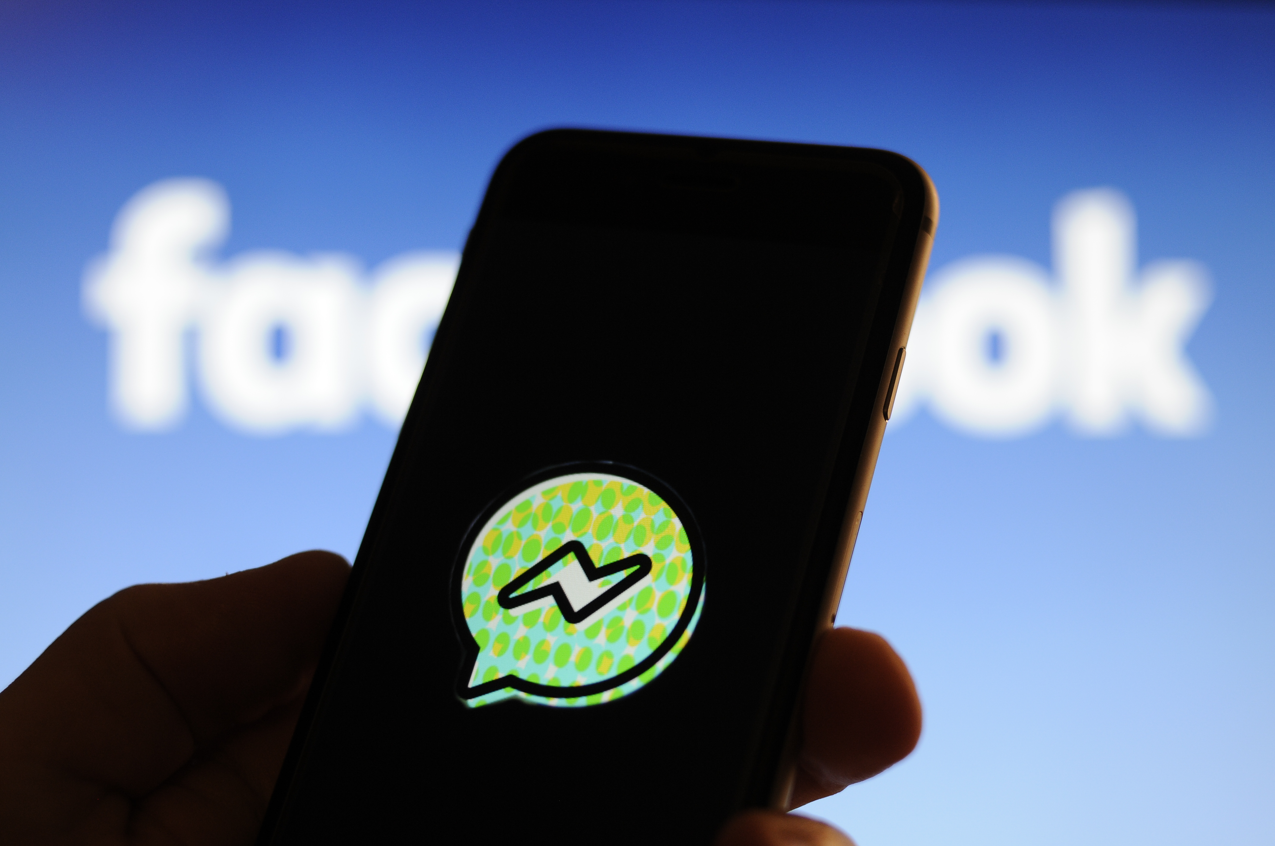 A user holds up a smartphone with the Facebook Messenger Kids application logo.