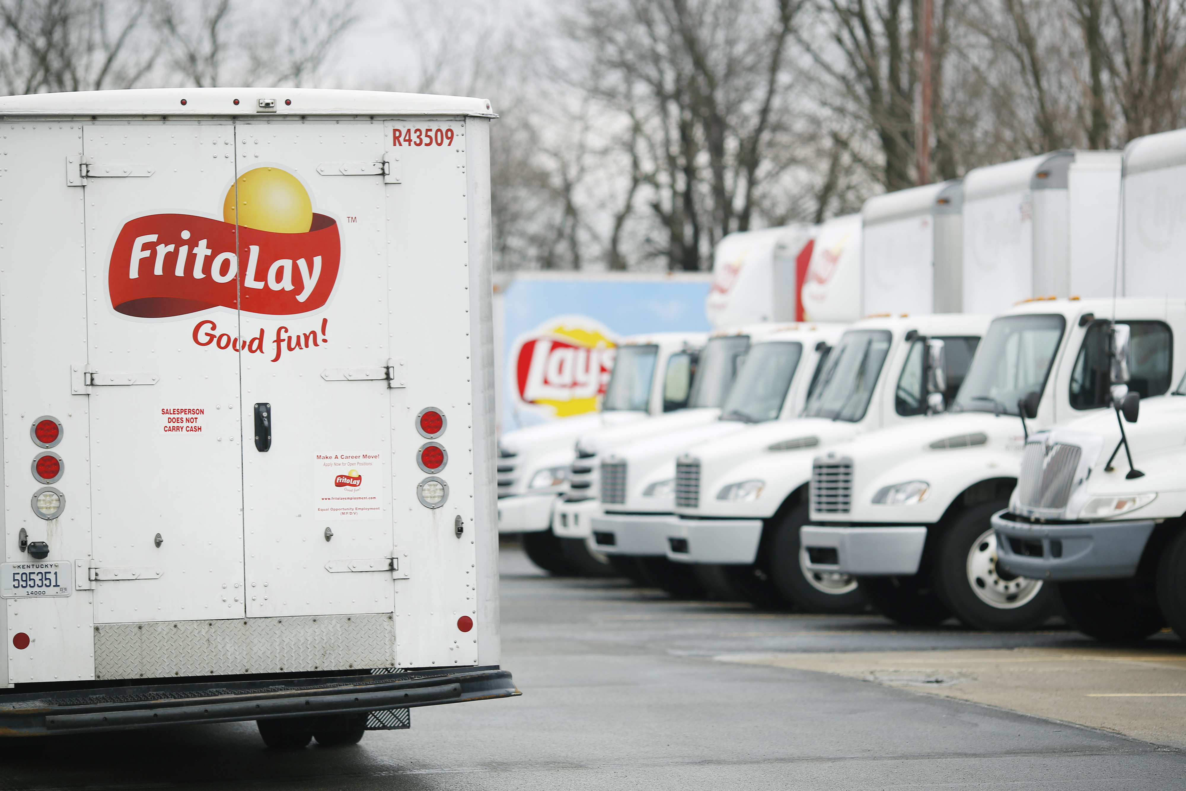 Delivery trucks with PepsiCo Inc. Frito Lay branding sit parked outside a distribution facility