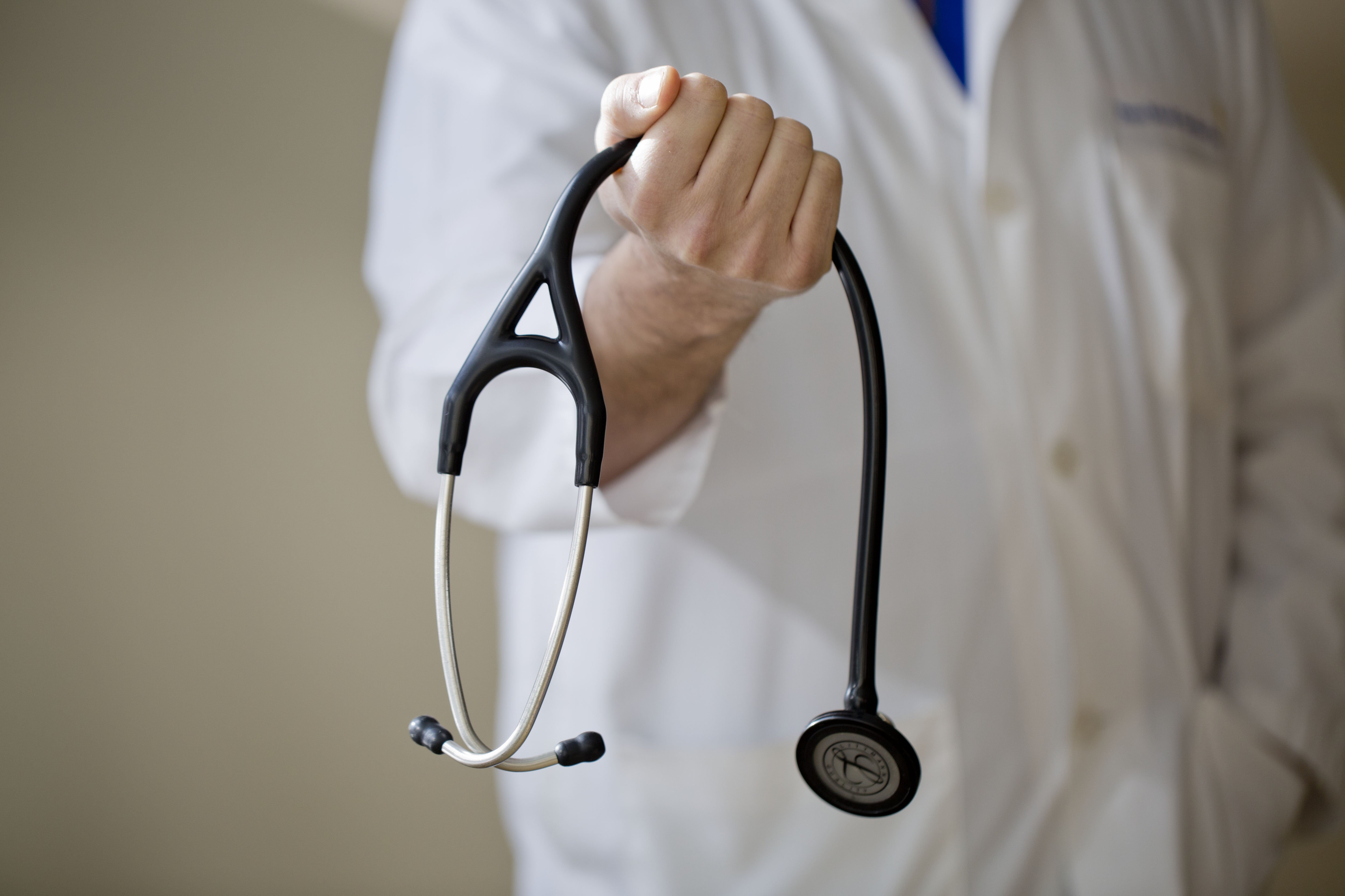 Doctor in white lab coat grips stethoscope