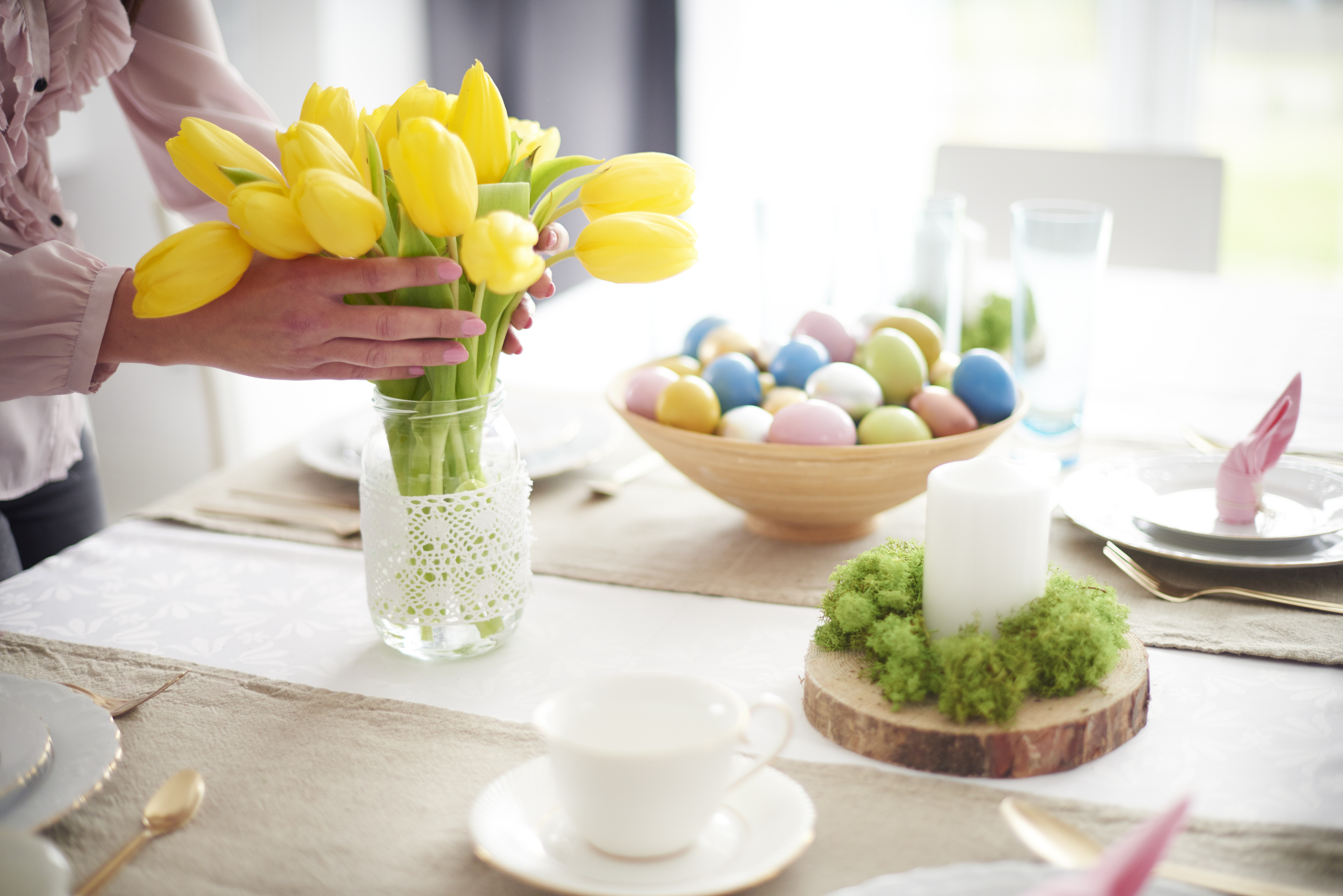 Hands of woman arranging yellow tulips at easter dining table
