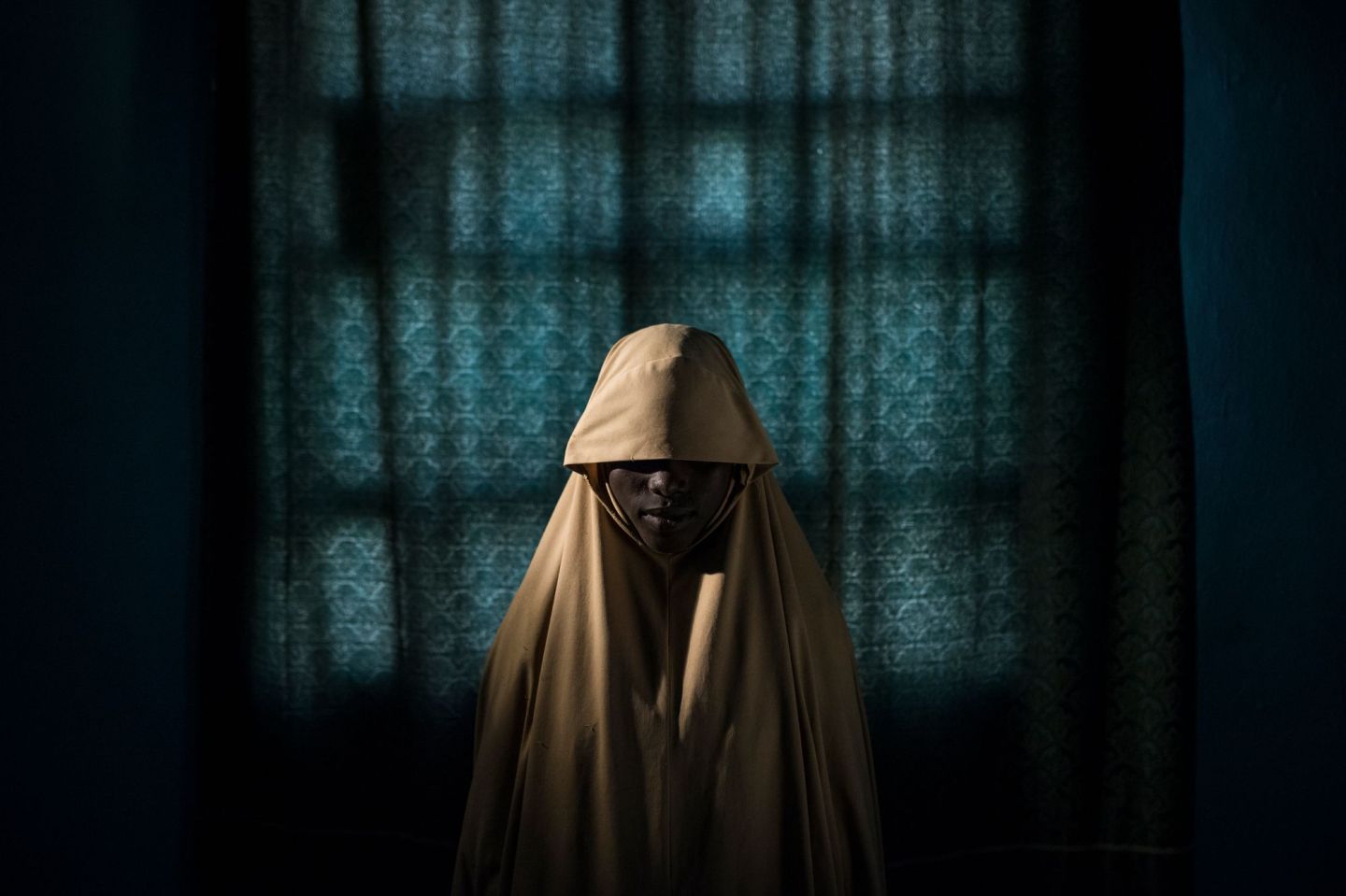 Aisha, age 14, stands for a portrait in Maiduguri, Borno State, Nigeria on Sept. 21, 2017. Aisha was kidnapped by Boko Haram then assigned a suicide bombing mission. After she was strapped with explosives, she found help instead of blowing herself and others up. Photo by Adam Ferguson for The New York Times