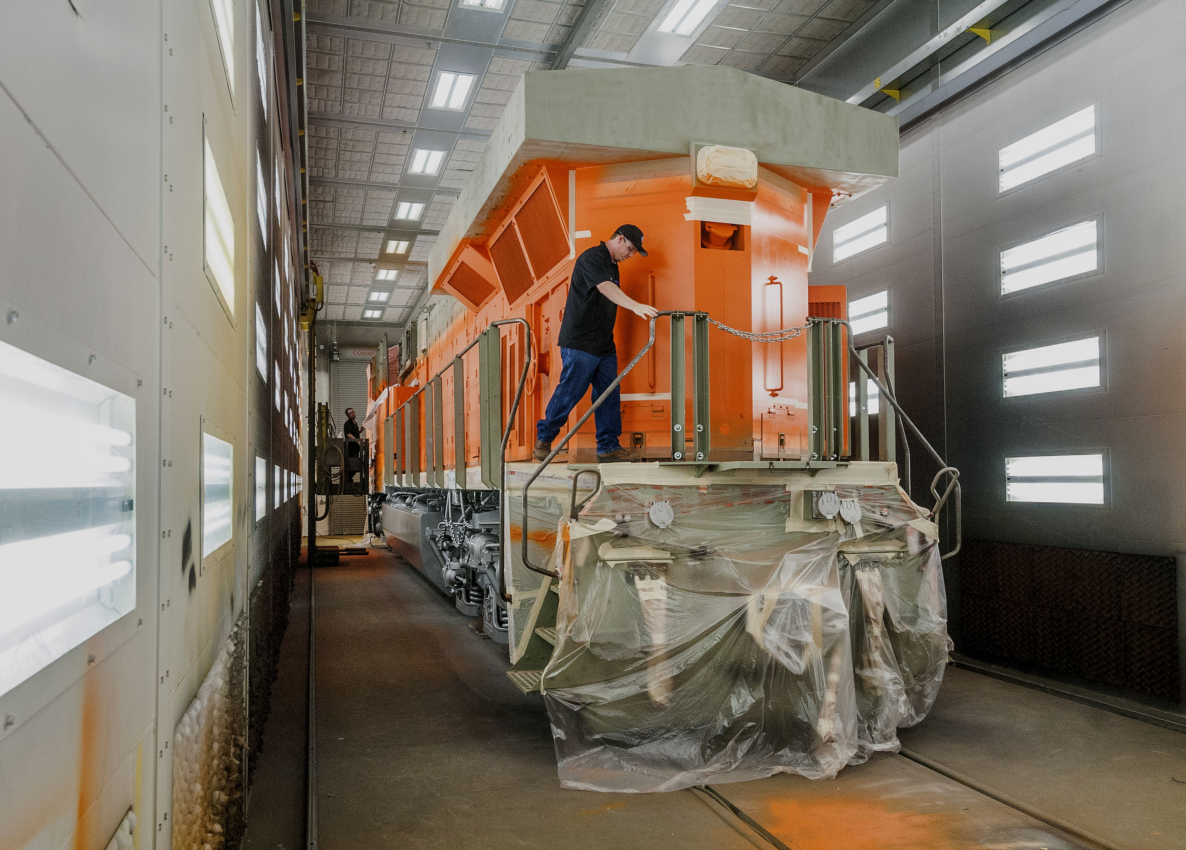 A man works on a bright orange diesel locomotive at a GE facility.