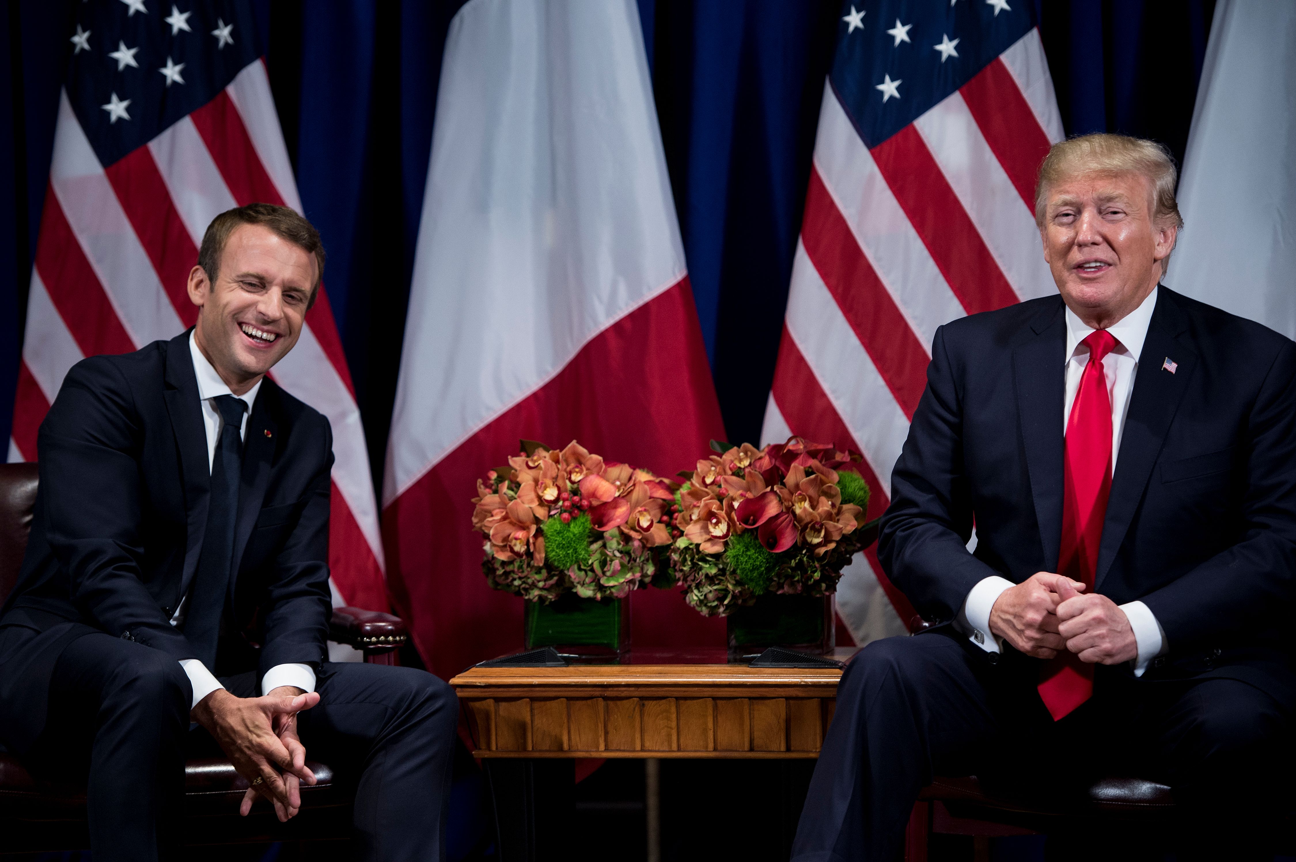 Emmanuel Macron and Donald Trump laugh as they sit next to one another.