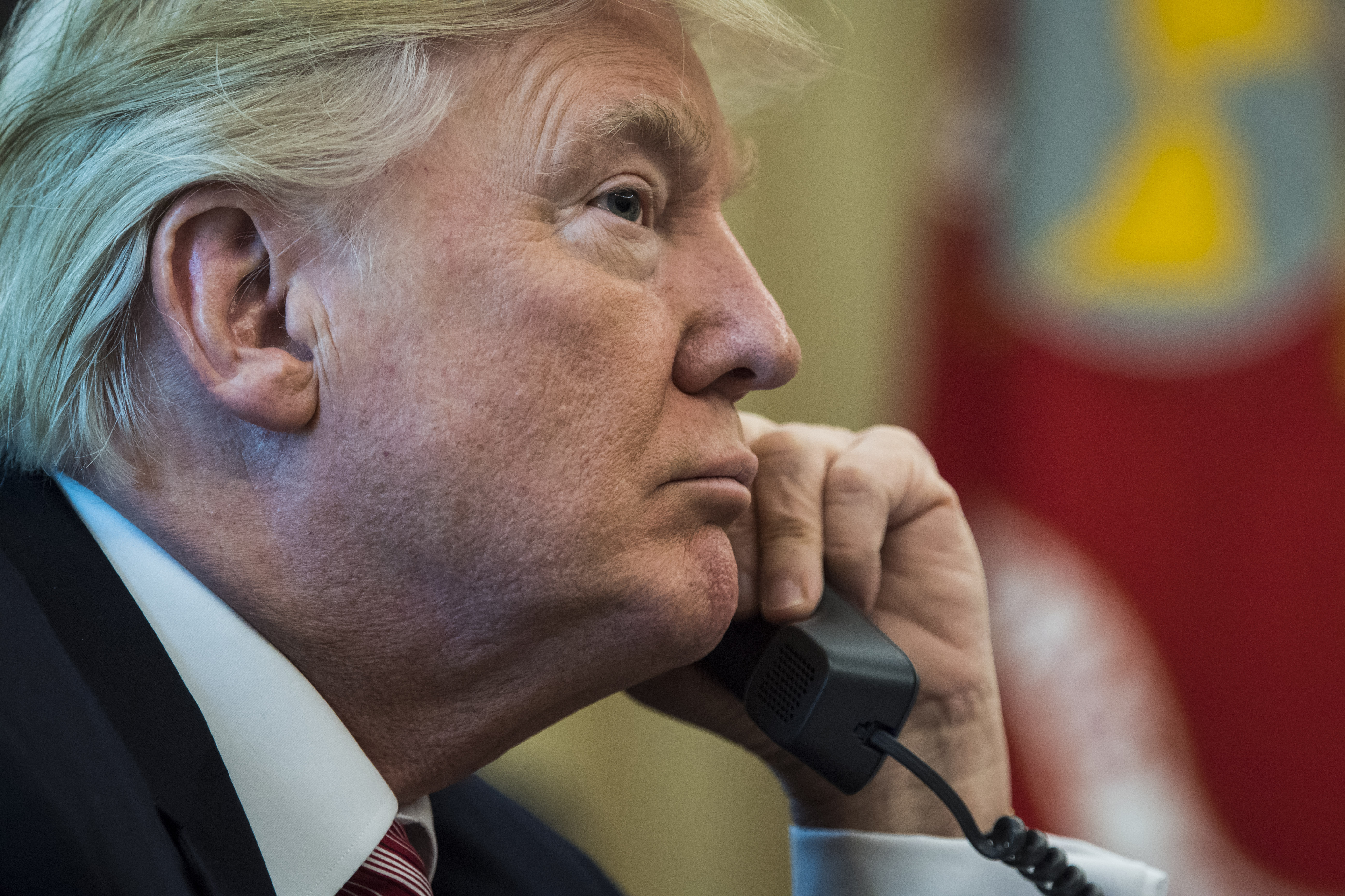 President Donald Trump holds a phone up to his left ear with the right side of his face in profile.