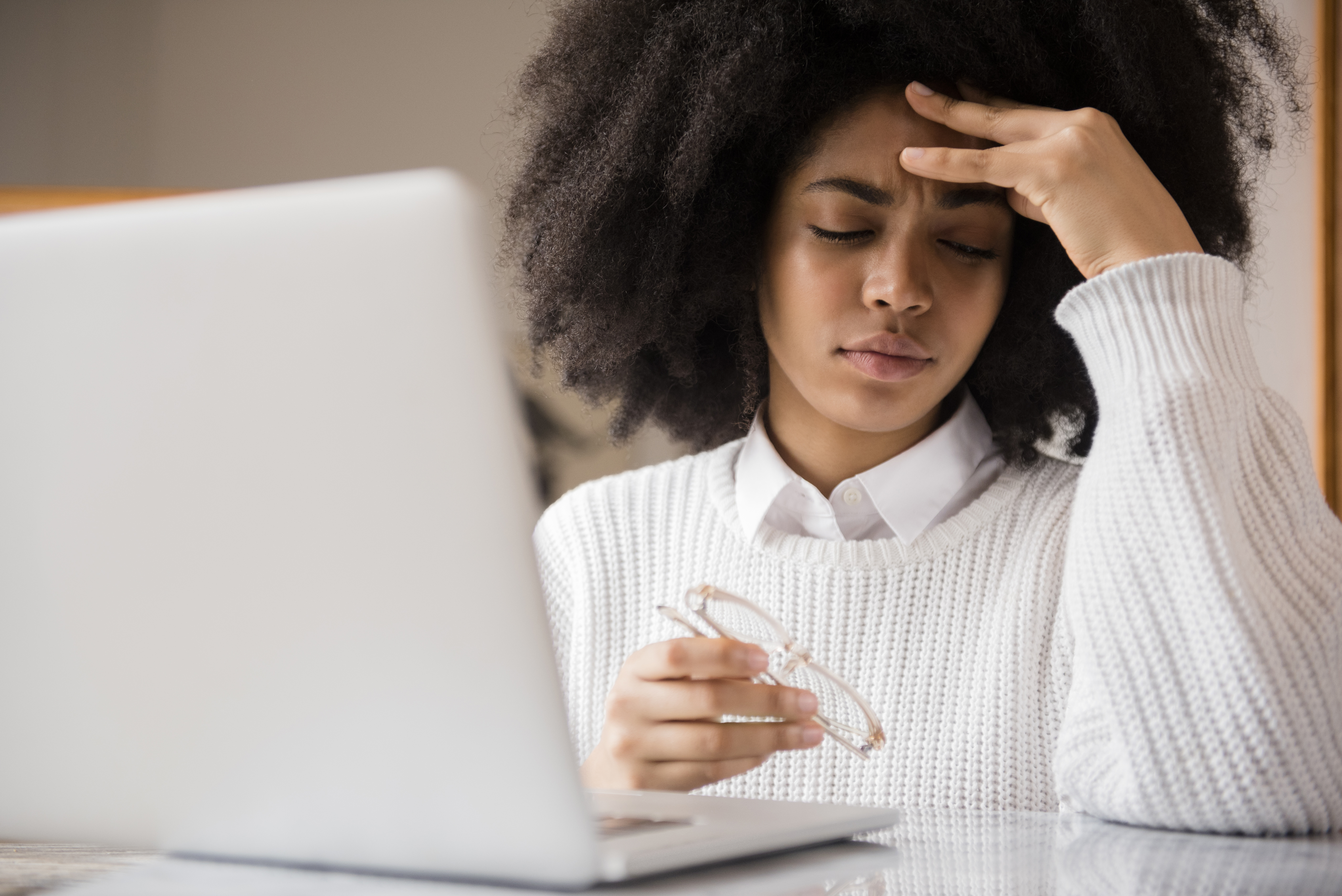 Frustrated woman holding eyeglasses at her laptop.
