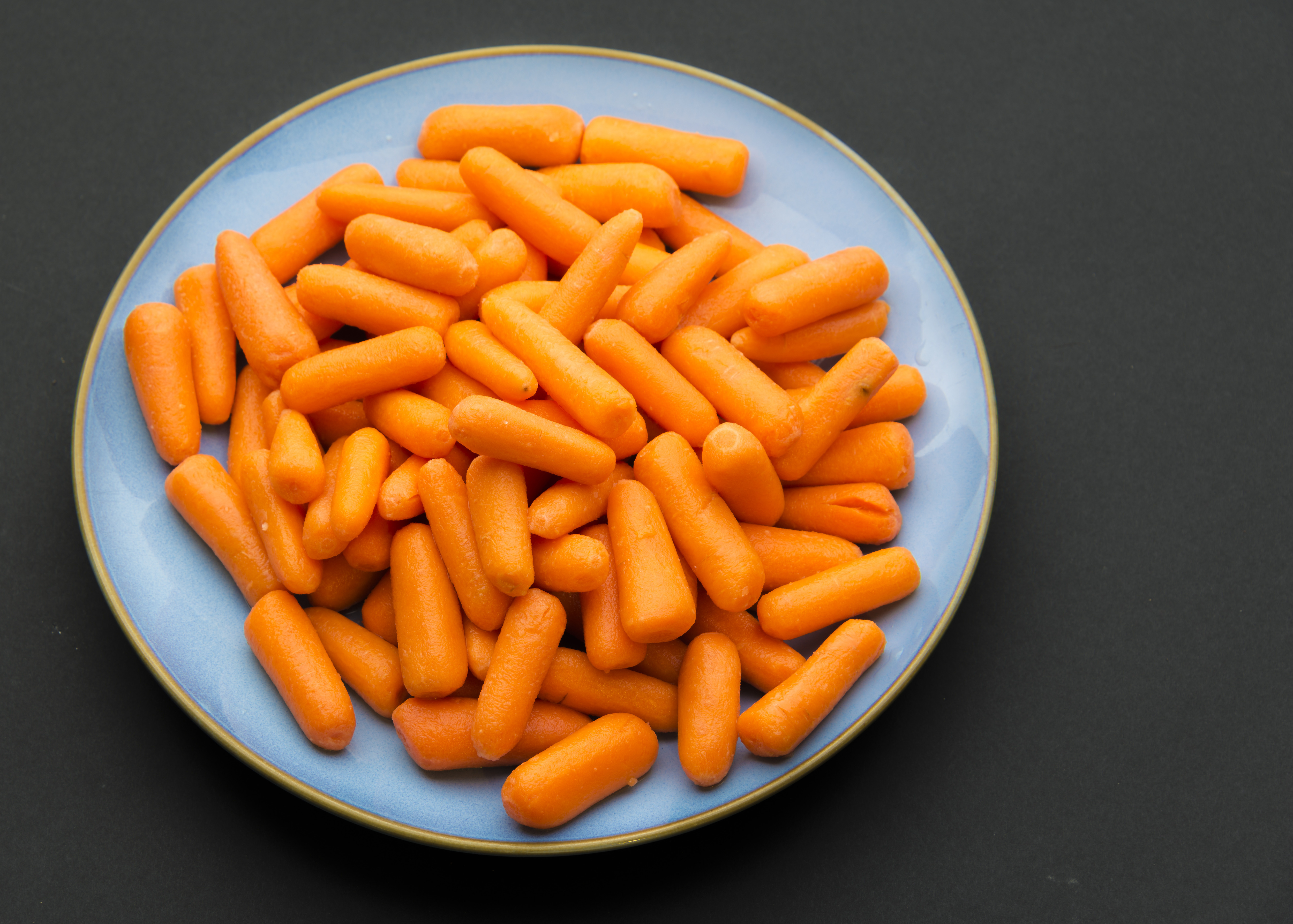 Baby carrots placed in blue plate against black background