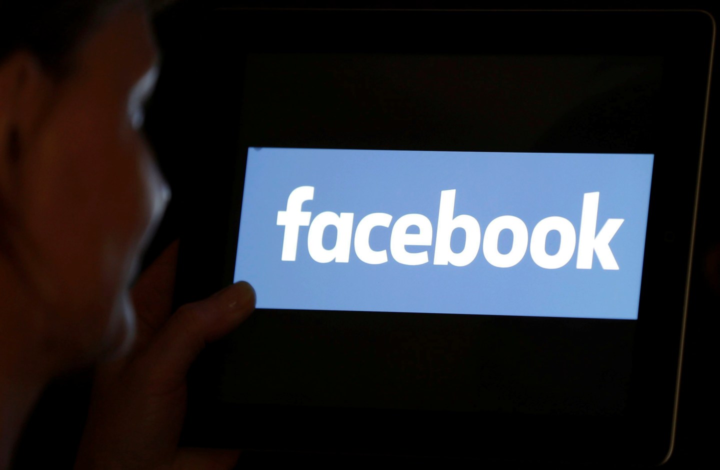 A woman looks at the Facebook logo on an iPad in this photo illustration