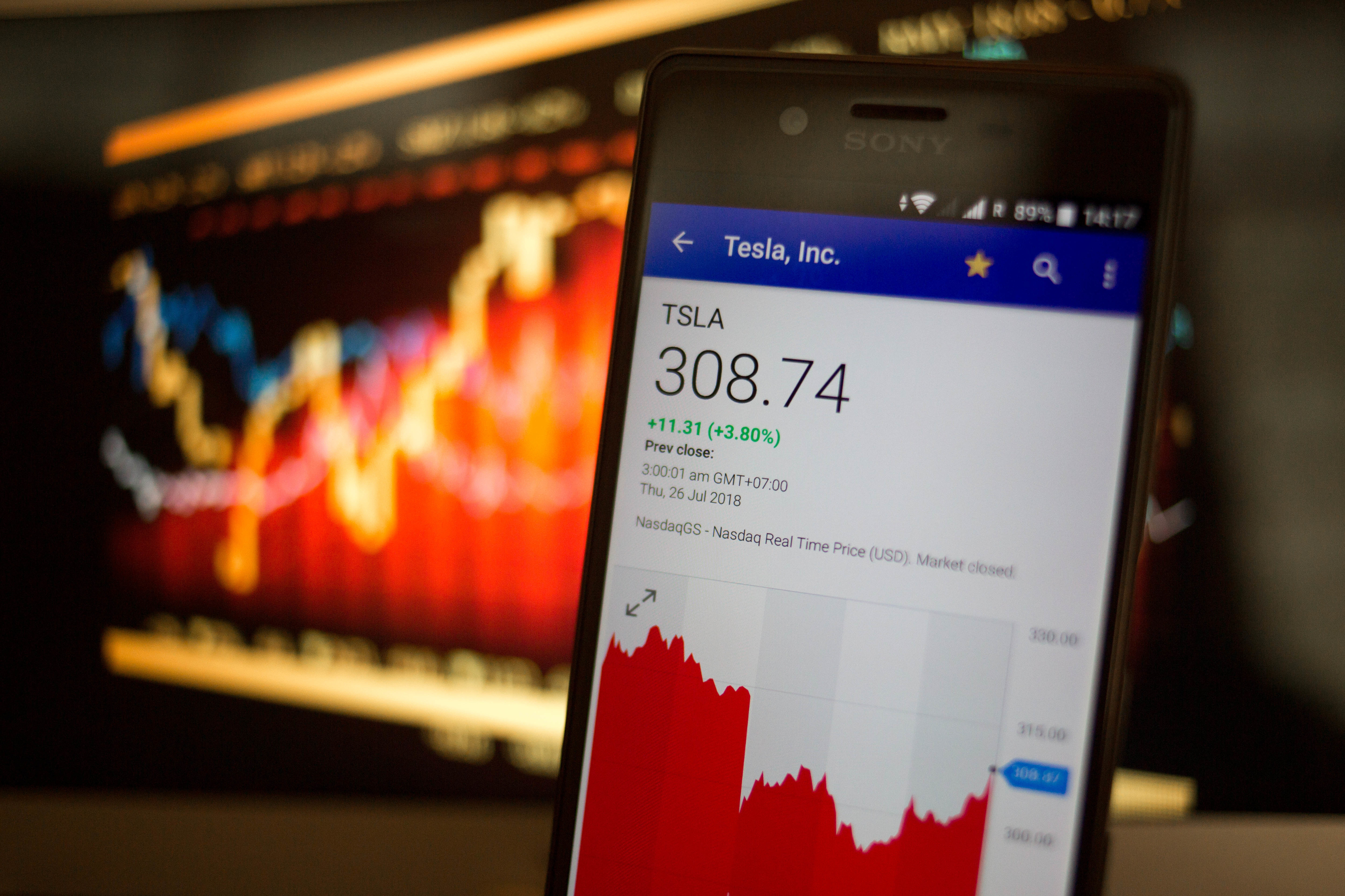 A smartphone displays the Tesla, Inc. market value on the
