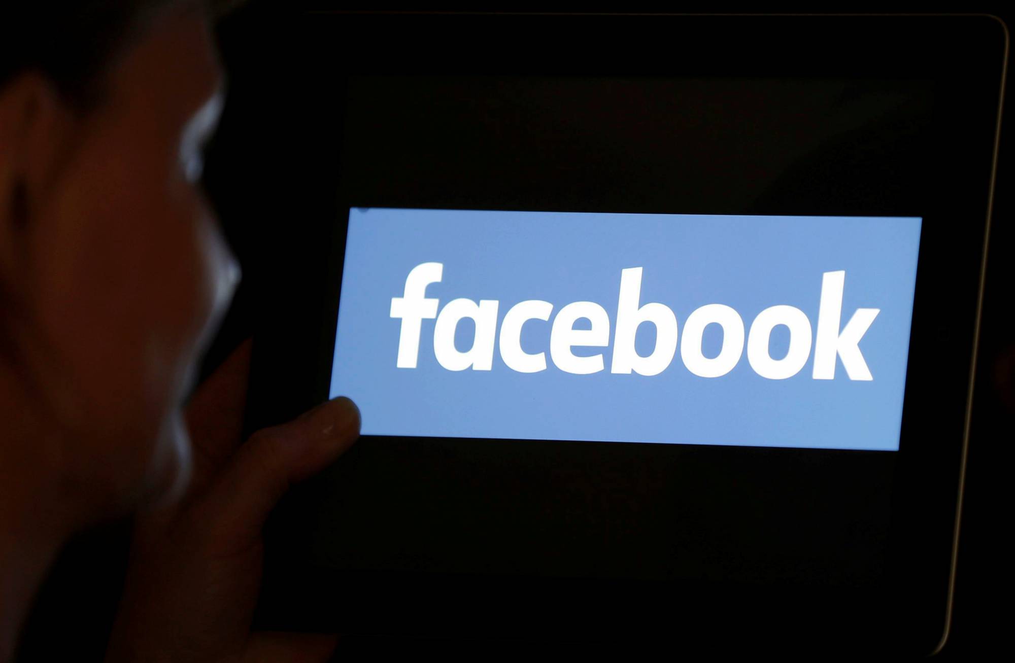 A woman looks at the Facebook logo on an iPad in this photo illustration