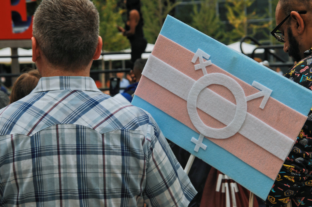 man stands with his back to the camera holding a trans flag